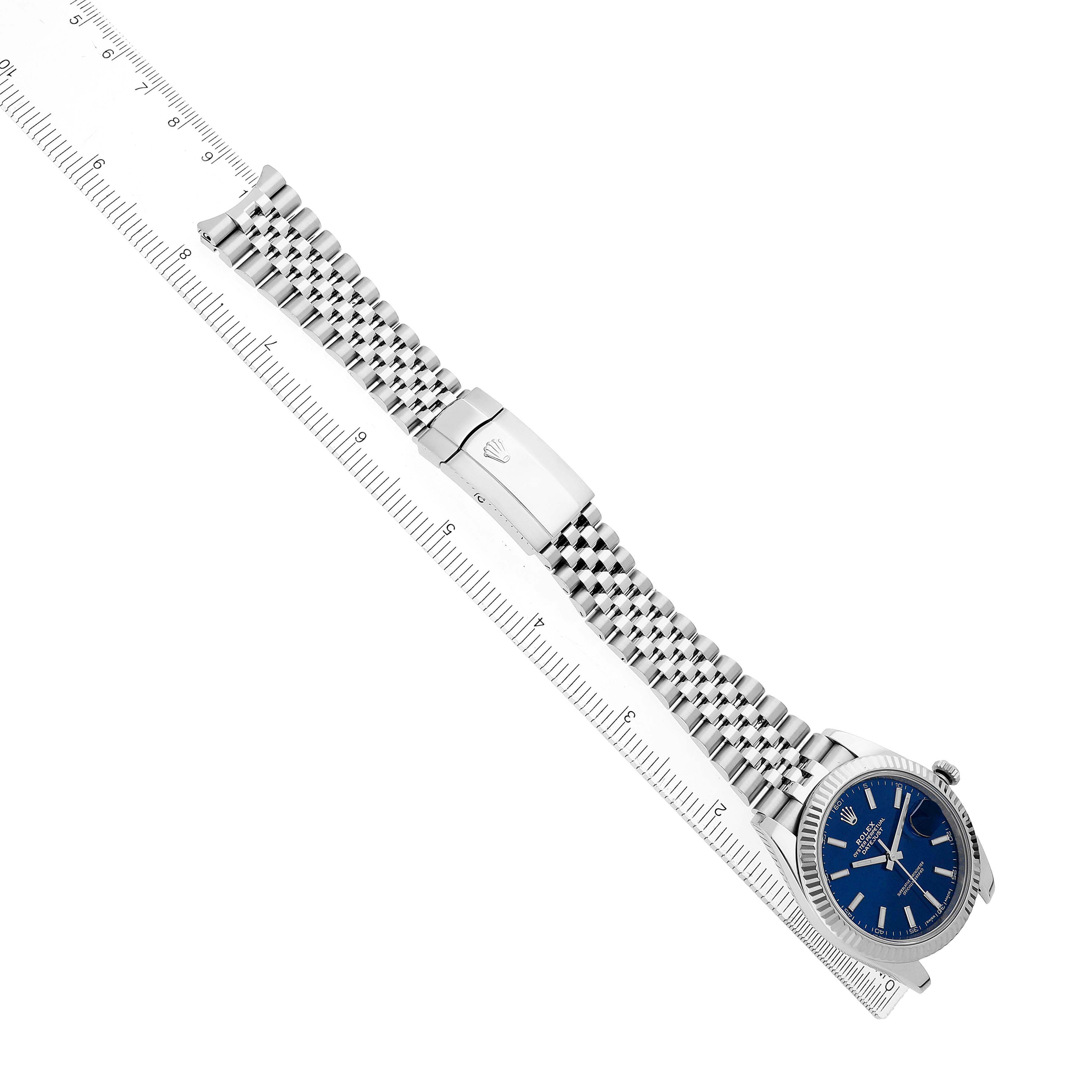 The Rolex Datejust 41 126334 Men's Stainless Steel Blue Dial watch is shown diagonally, highlighting its bracelet, clasp, and blue dial next to a ruler.