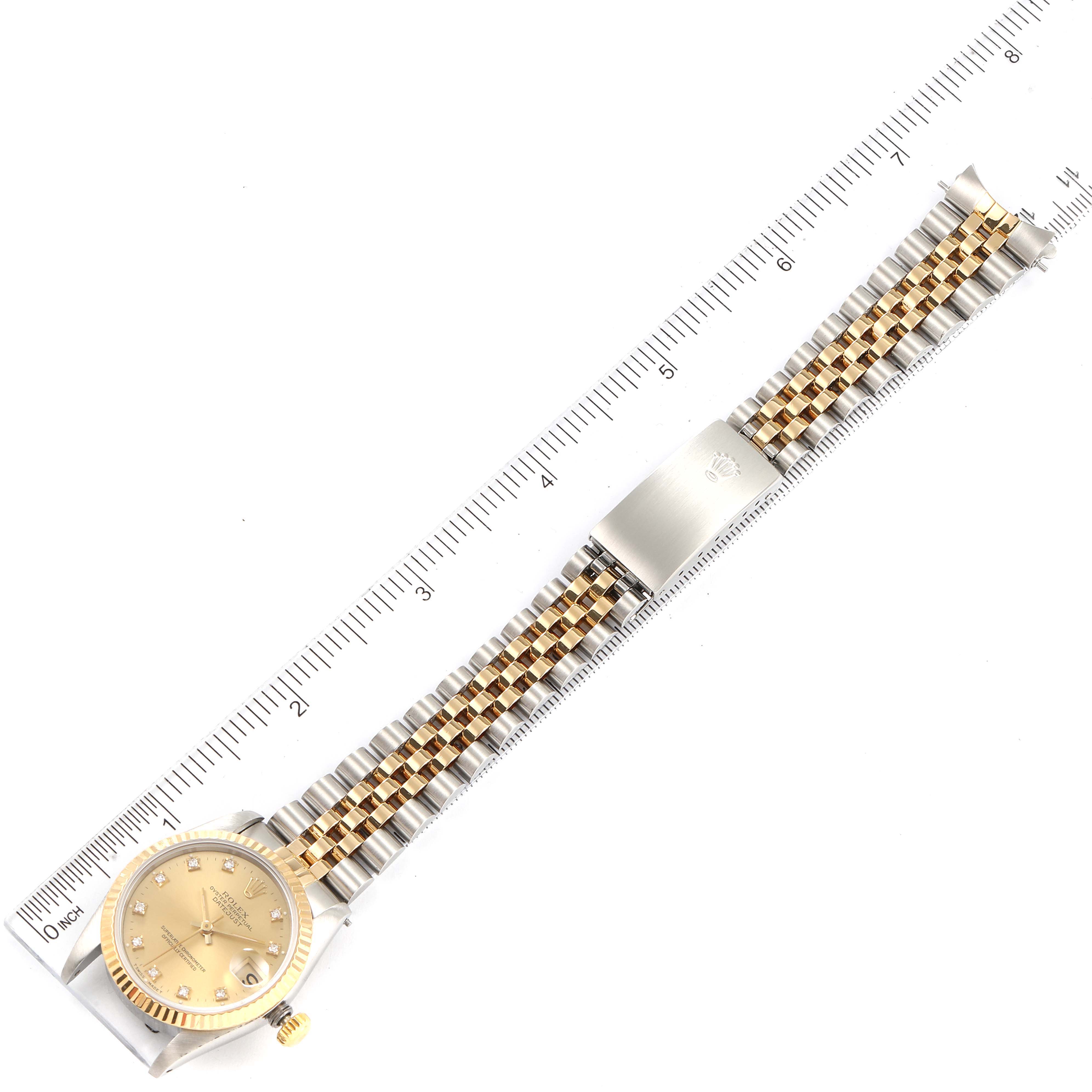 The image shows a top-down view of a mid-size Rolex watch, featuring its gold dial, bezel, and two-tone metal bracelet with a clasp.