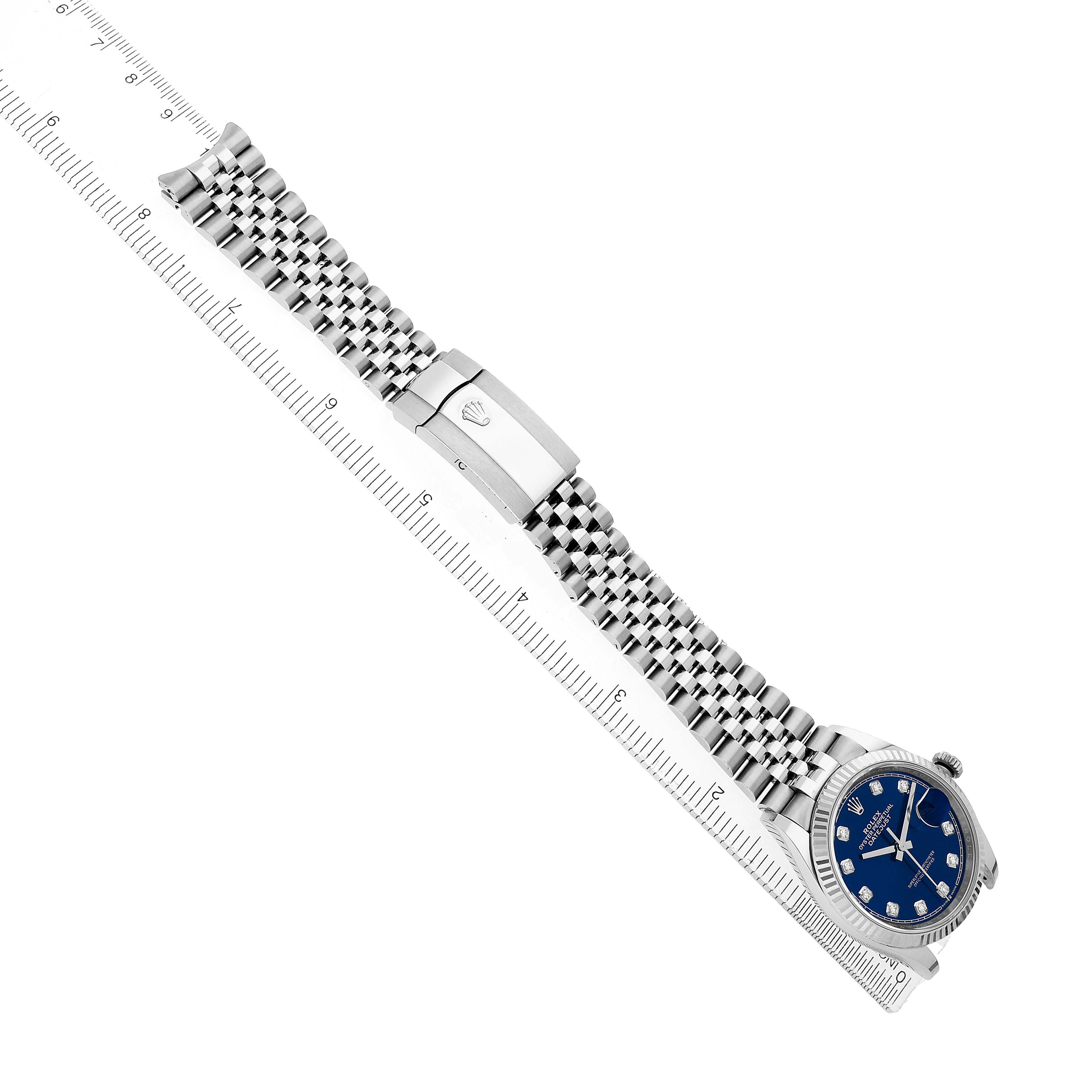 The Rolex Datejust 126234 Men's Stainless Steel Blue Dial watch is shown from a top view, displaying its face, bracelet, and clasp alongside a ruler for scale.
