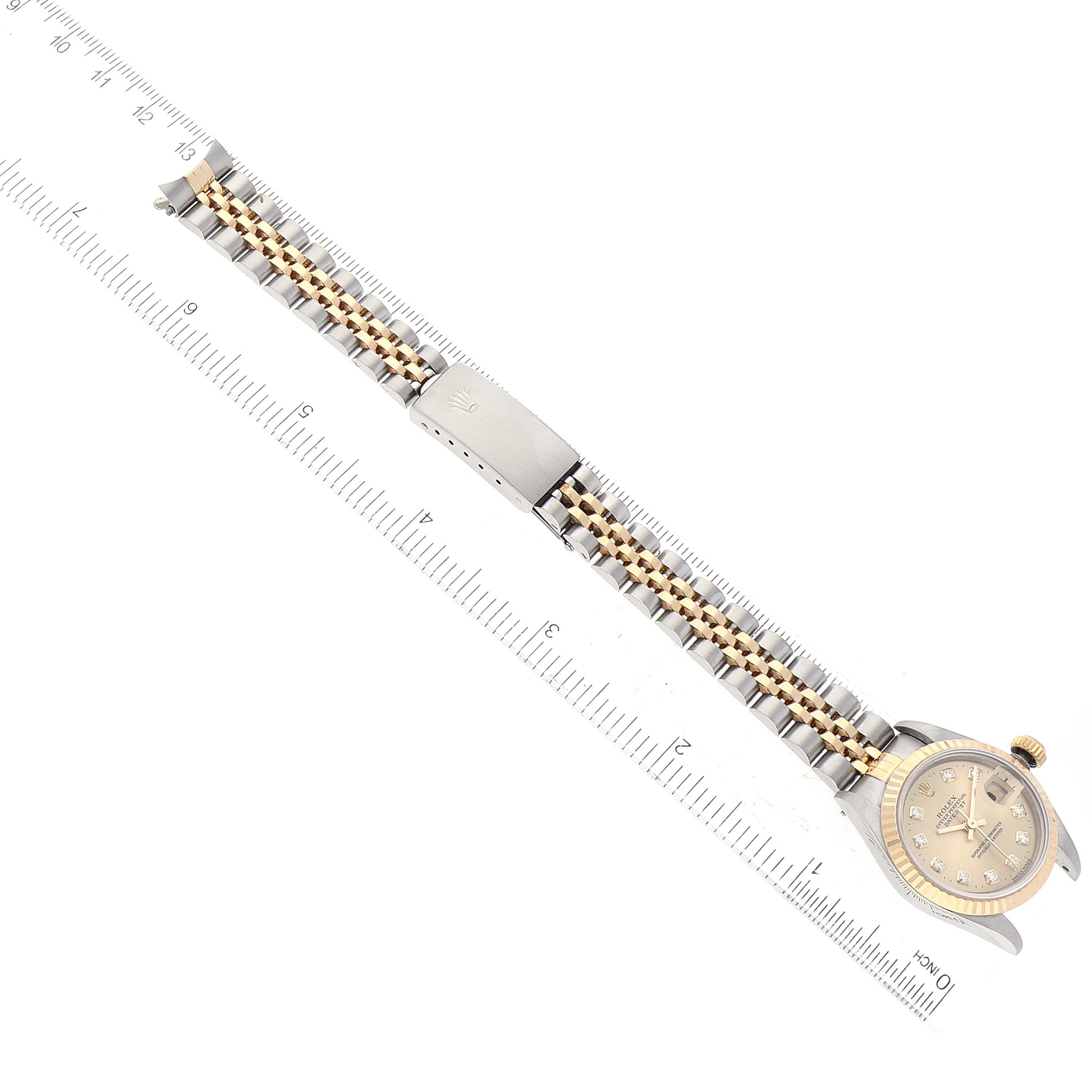 The Rolex Datejust 69173 Women's Steel and Gold (two tone) Champagne Dial 69173 Women's Steel and Gold (two tone) Champagne Dial watch is shown from an angled top-down view, highlighting its face, bezel, and two-tone bracelet alongside a ruler.