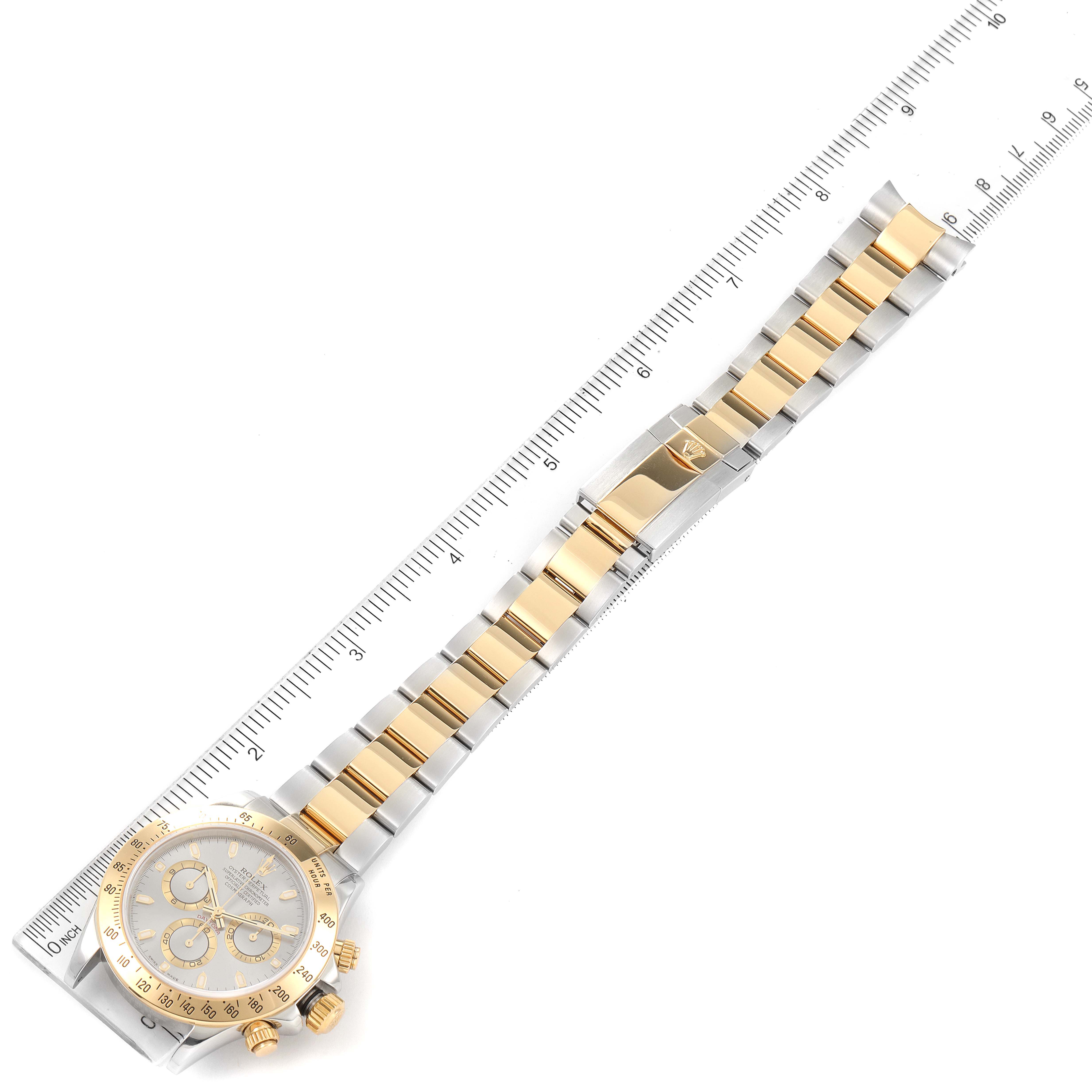 The image shows a full view of a Rolex Daytona 16523 Men's Steel and Gold (two tone) Grey Dial 16523 Men's Steel and Gold (two tone) Grey Dial watch laid flat with its band extended, alongside a ruler for scale.