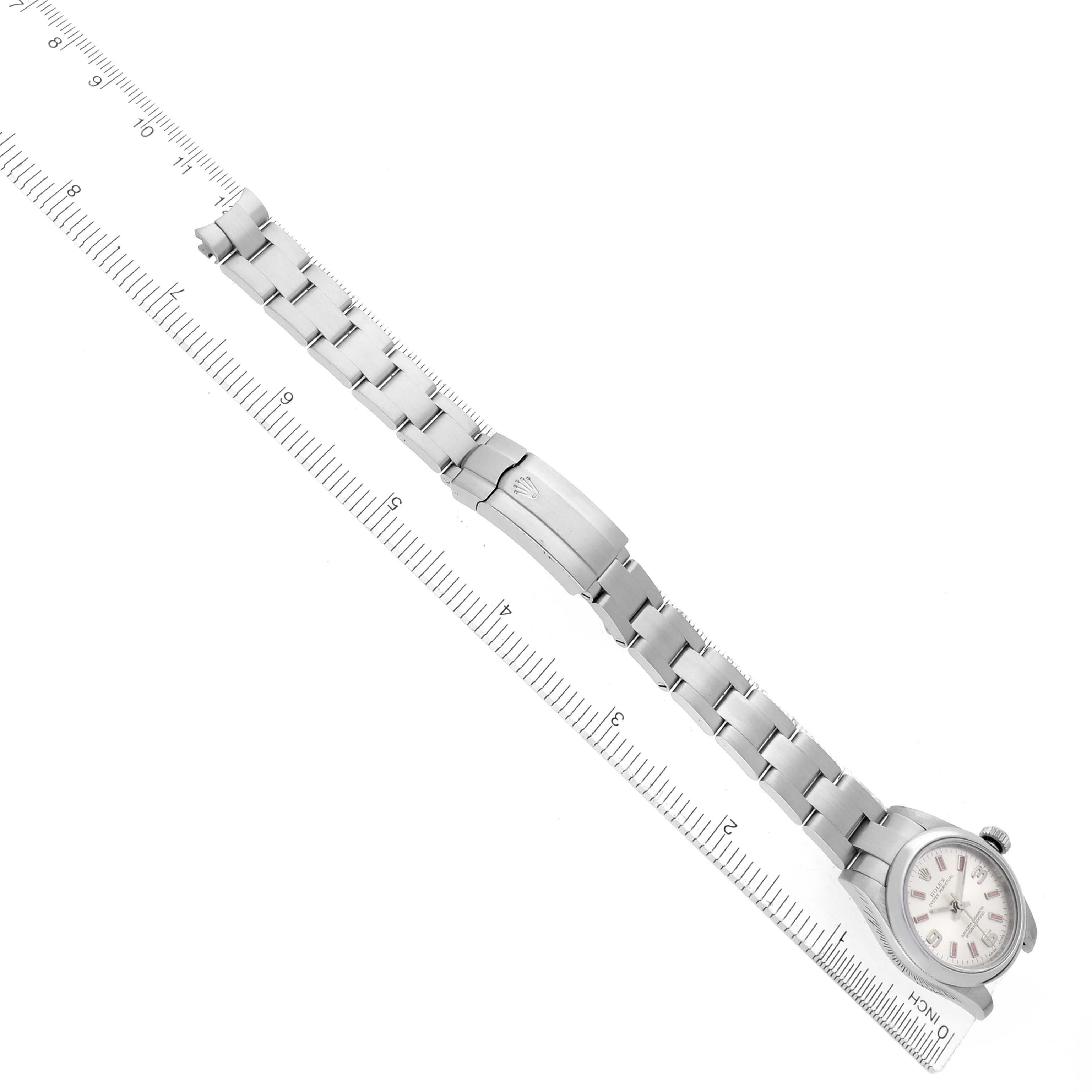 The image shows a Rolex Oyster Perpetual 176200 Women's Stainless Steel Silver Dial watch and its bracelet laid flat diagonally alongside a ruler.