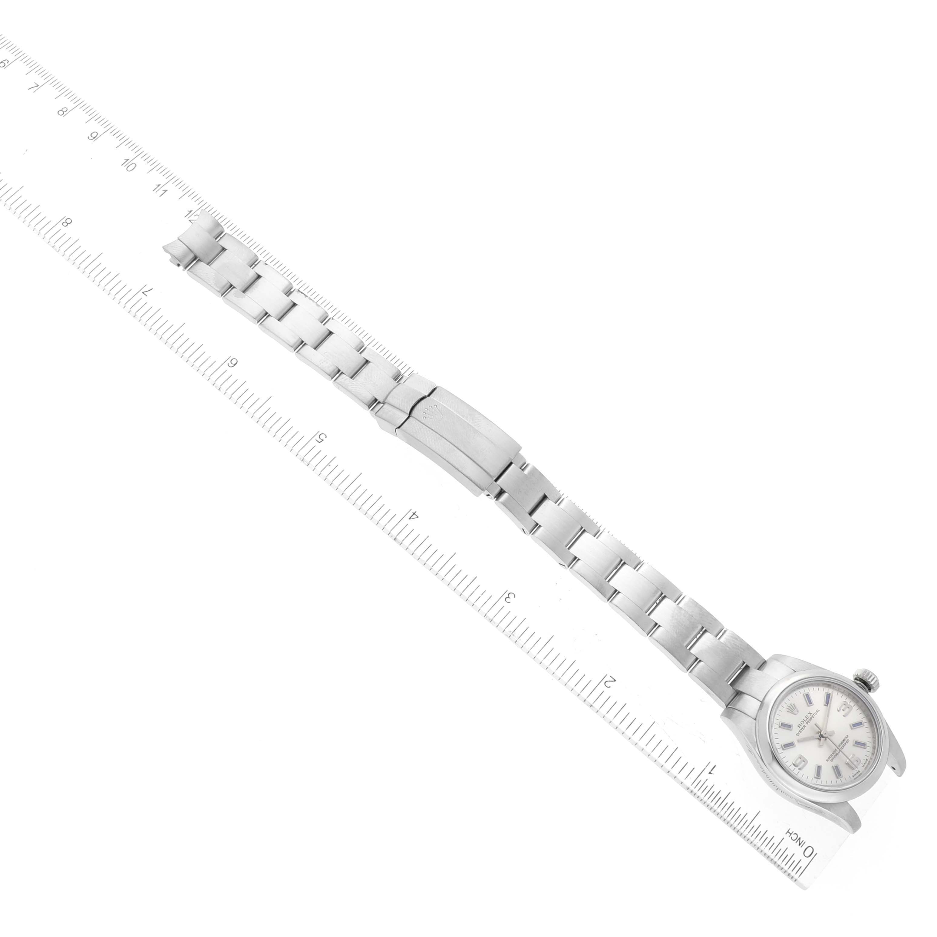 The image shows a Rolex Oyster Perpetual 176200 Women
s Stainless Steel Silver Dial 176200 Women
s Stainless Steel Silver Dial watch held next to a ruler, displaying the bracelet and case from an aerial view.