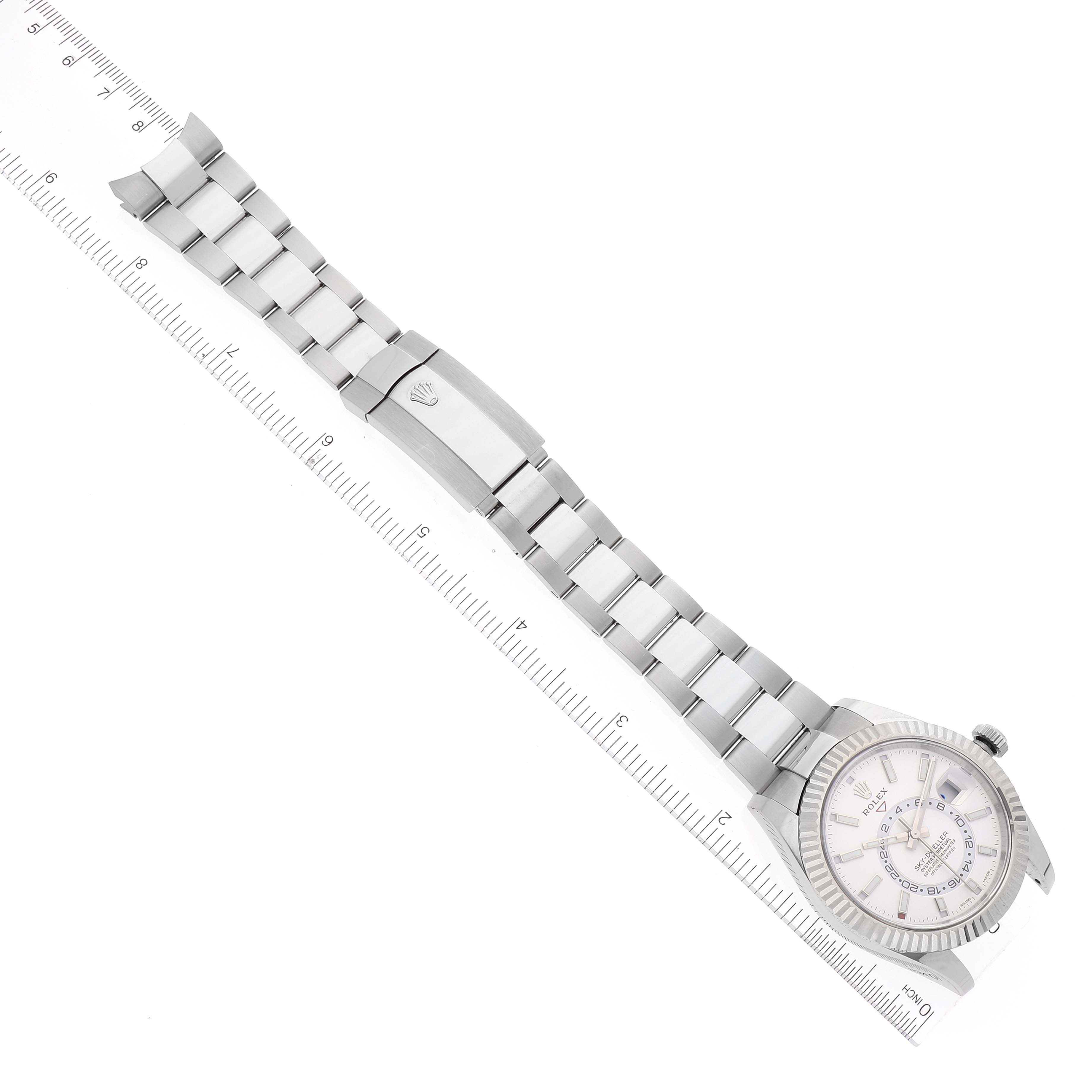 The image shows a Rolex Sky-Dweller 326934 Men's Stainless Steel White Dial 326934 Men's Stainless Steel White Dial watch laid flat with the bracelet and clasp visible, next to a measuring ruler for scale.