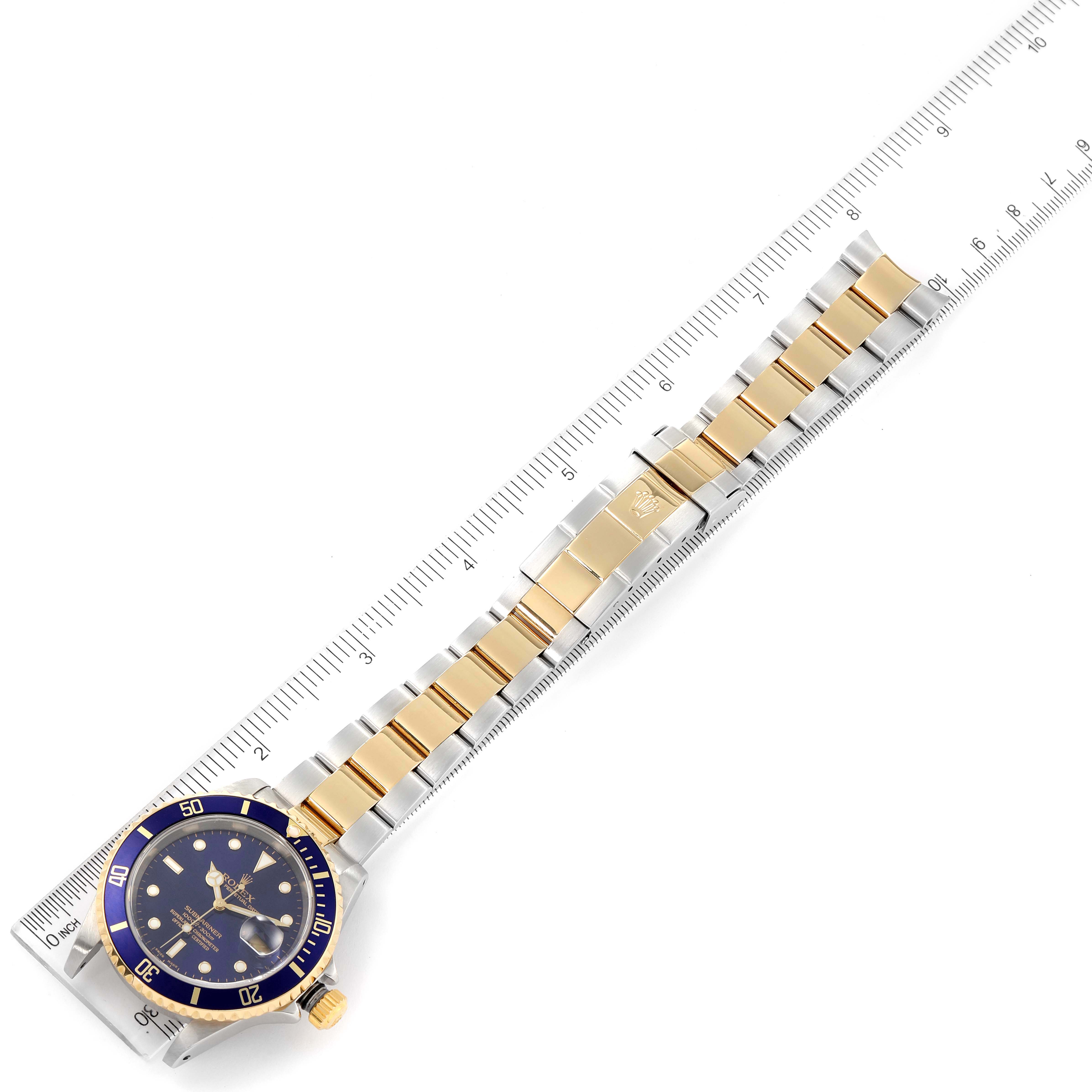 The image shows a Rolex Submariner 16613 Men's Steel and Gold (two tone) Blue Dial 16613 Men's Steel and Gold (two tone) Blue Dial watch, with its face and two-tone metal band laid flat next to a ruler.