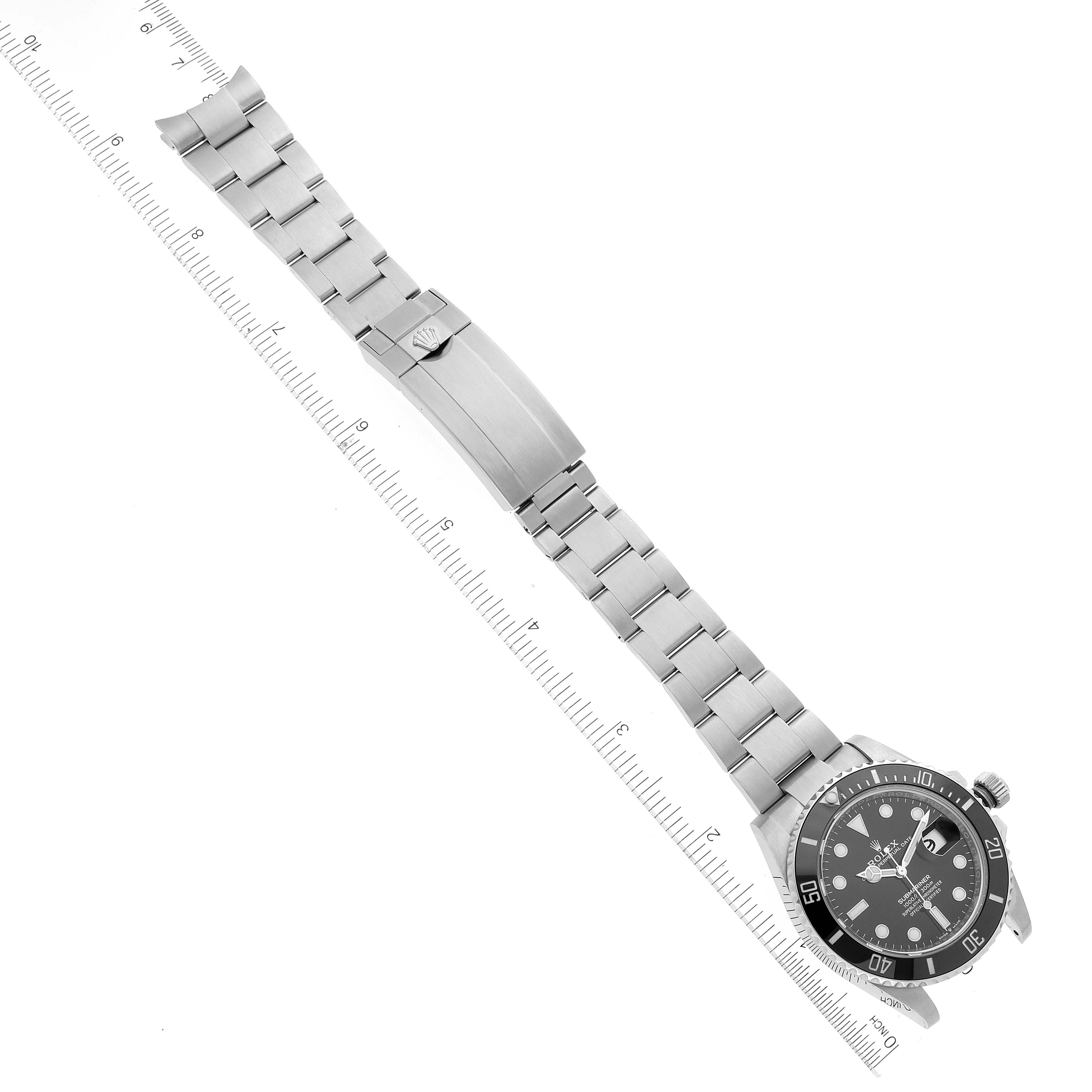 This image shows the Rolex Submariner 126610 Men
s Stainless Steel Black Dial 126610 Men
s Stainless Steel Black Dial watch laid flat, displaying its face, bezel, bracelet, and clasp alongside a ruler.