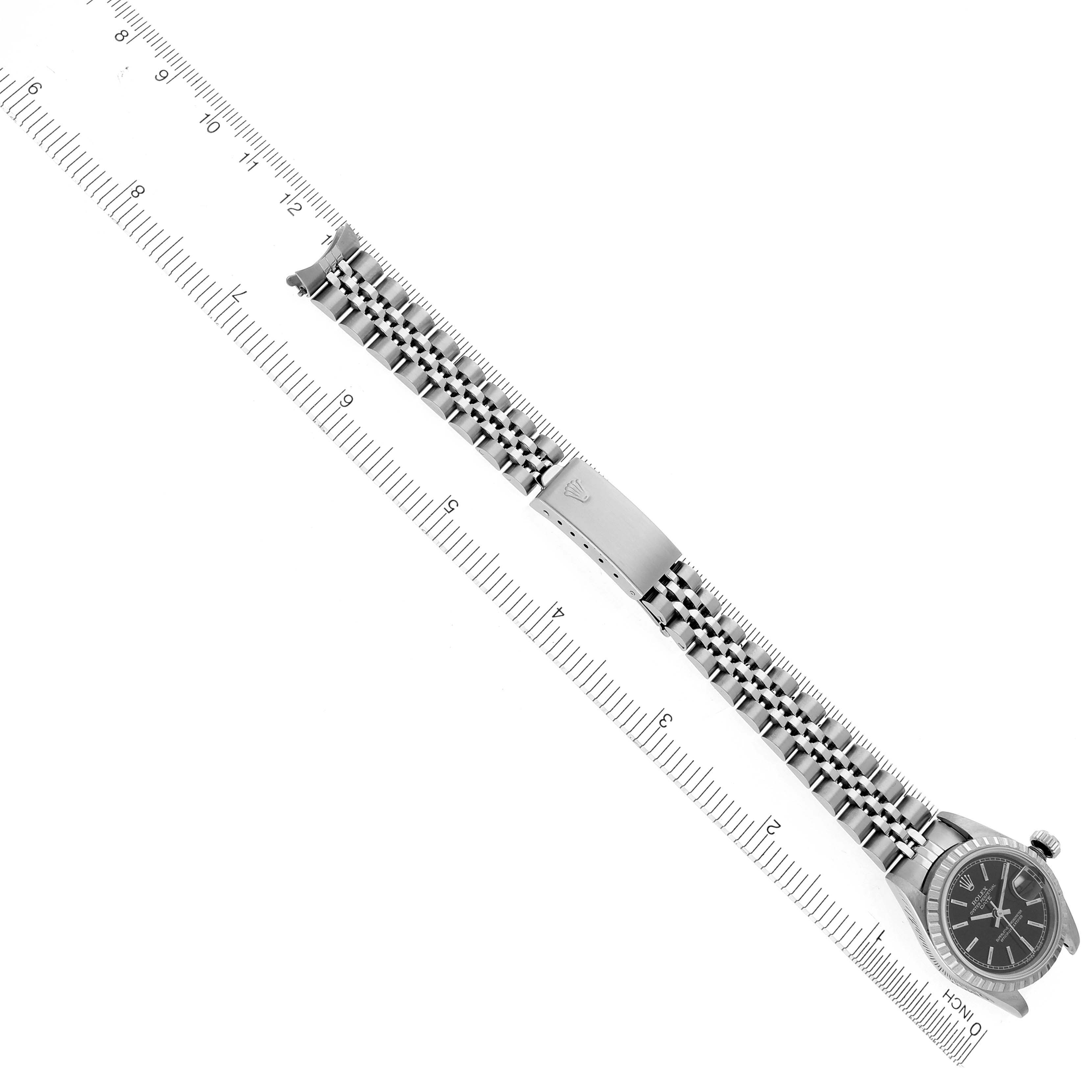 The Rolex Date 69240 Women's Stainless Steel Black Dial 69240 Women's Stainless Steel Black Dial watch is shown from a top view, displaying the face, jubilee bracelet, and clasp against a ruler for scale.