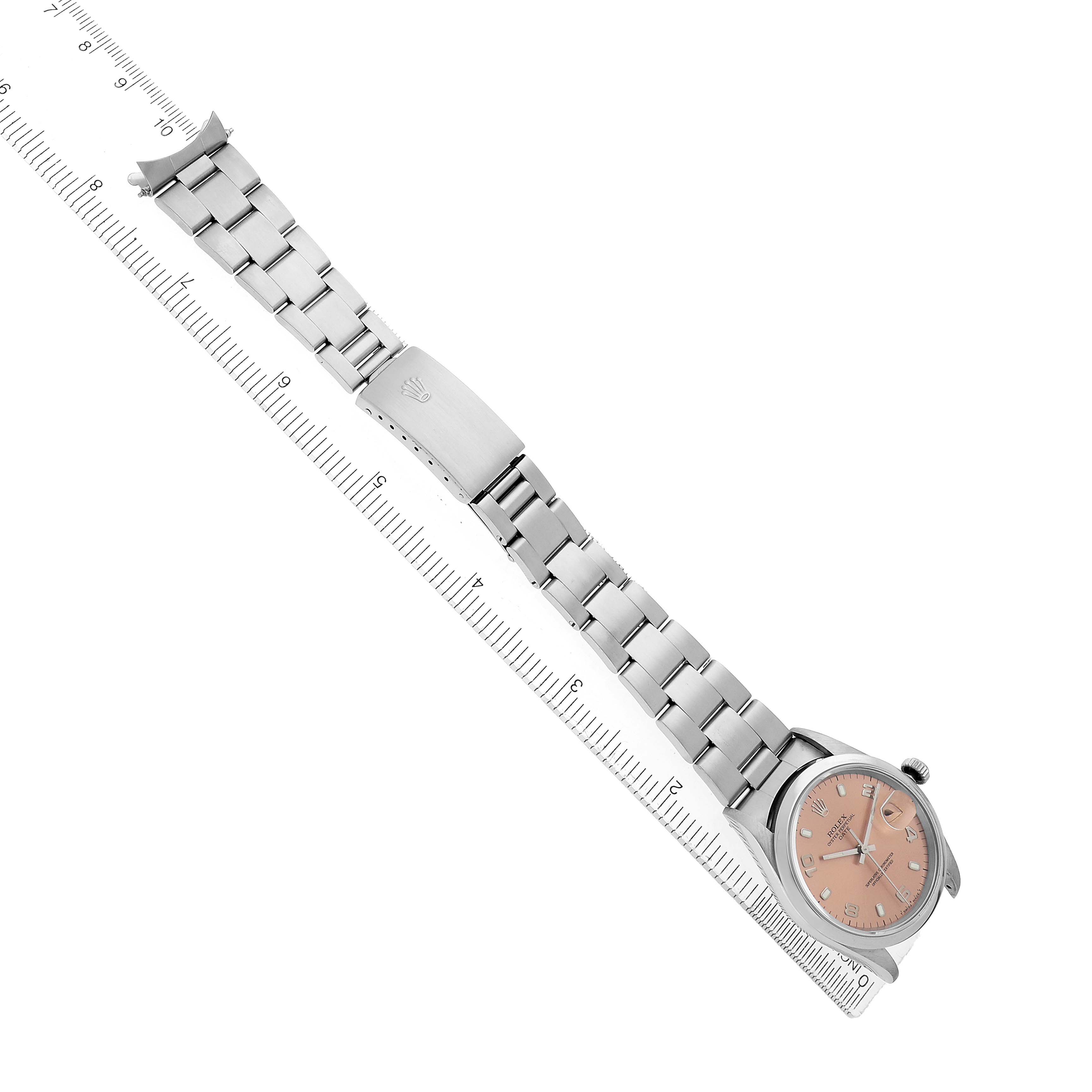 The image shows a Rolex Date 15200 Men's Stainless Steel Pink Dial model watch placed diagonally, displaying the bracelet, clasp, and face next to a ruler.