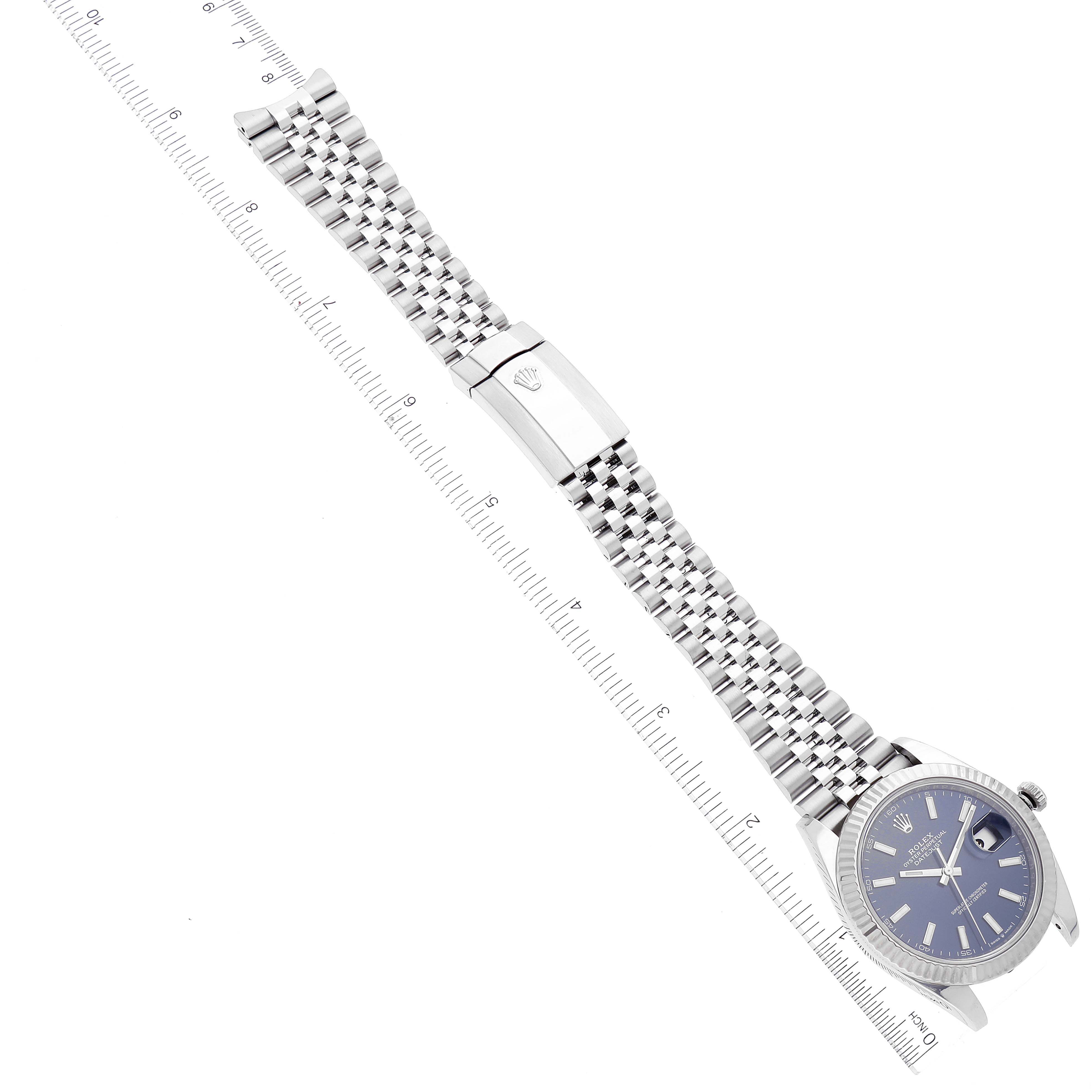 The Rolex Datejust 41 126334 Men's Stainless Steel Blue Dial 126334 Men's Stainless Steel Blue Dial watch is shown at a diagonal angle, displaying its face, bezel, and entire metal bracelet alongside a measuring ruler.