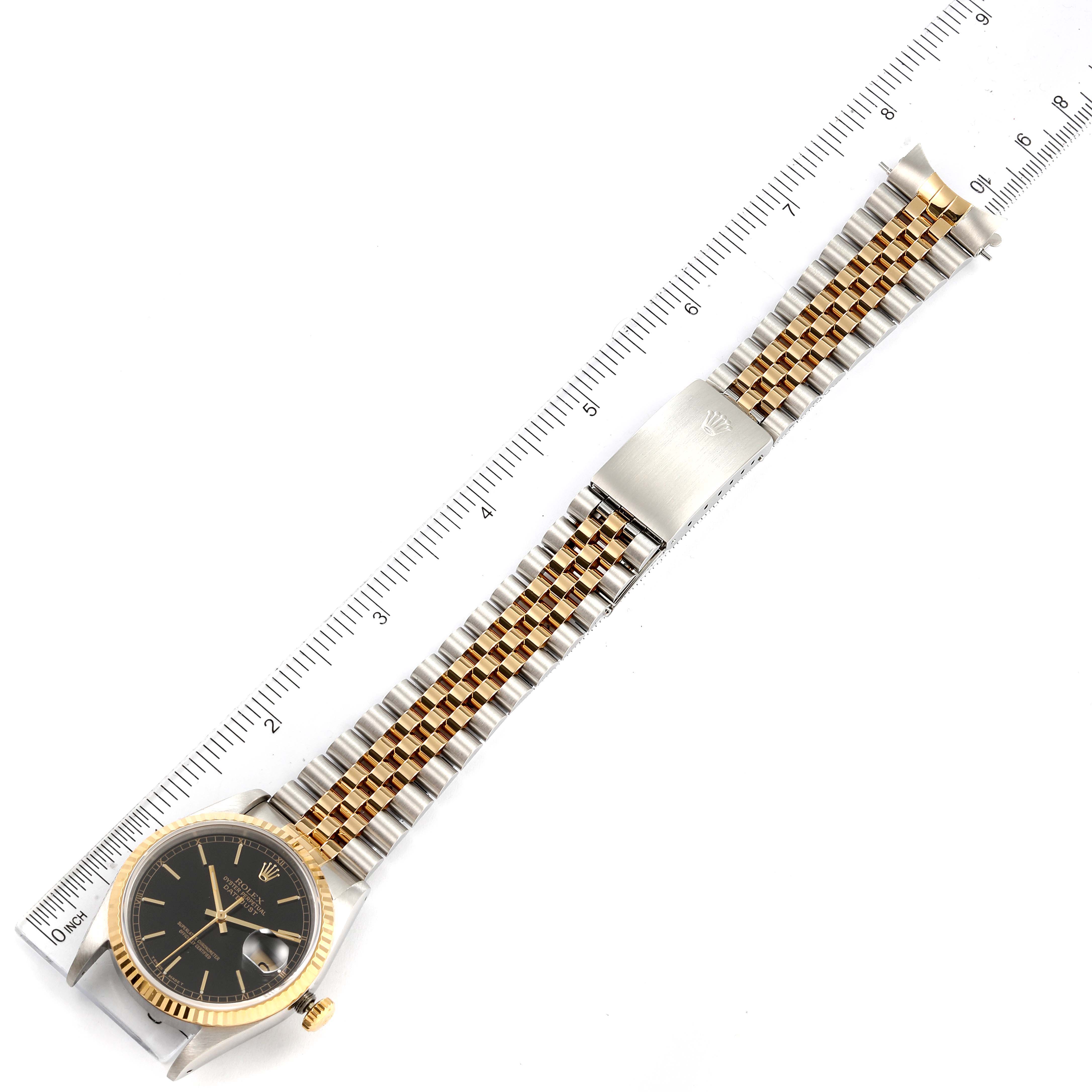The Rolex Datejust 16233 Men's Steel and Gold (two tone) Black Dial 16233 Men's Steel and Gold (two tone) Black Dial watch is shown from a top-down angle, displaying the face, bezel, bracelet, and clasp, alongside a measurement ruler.