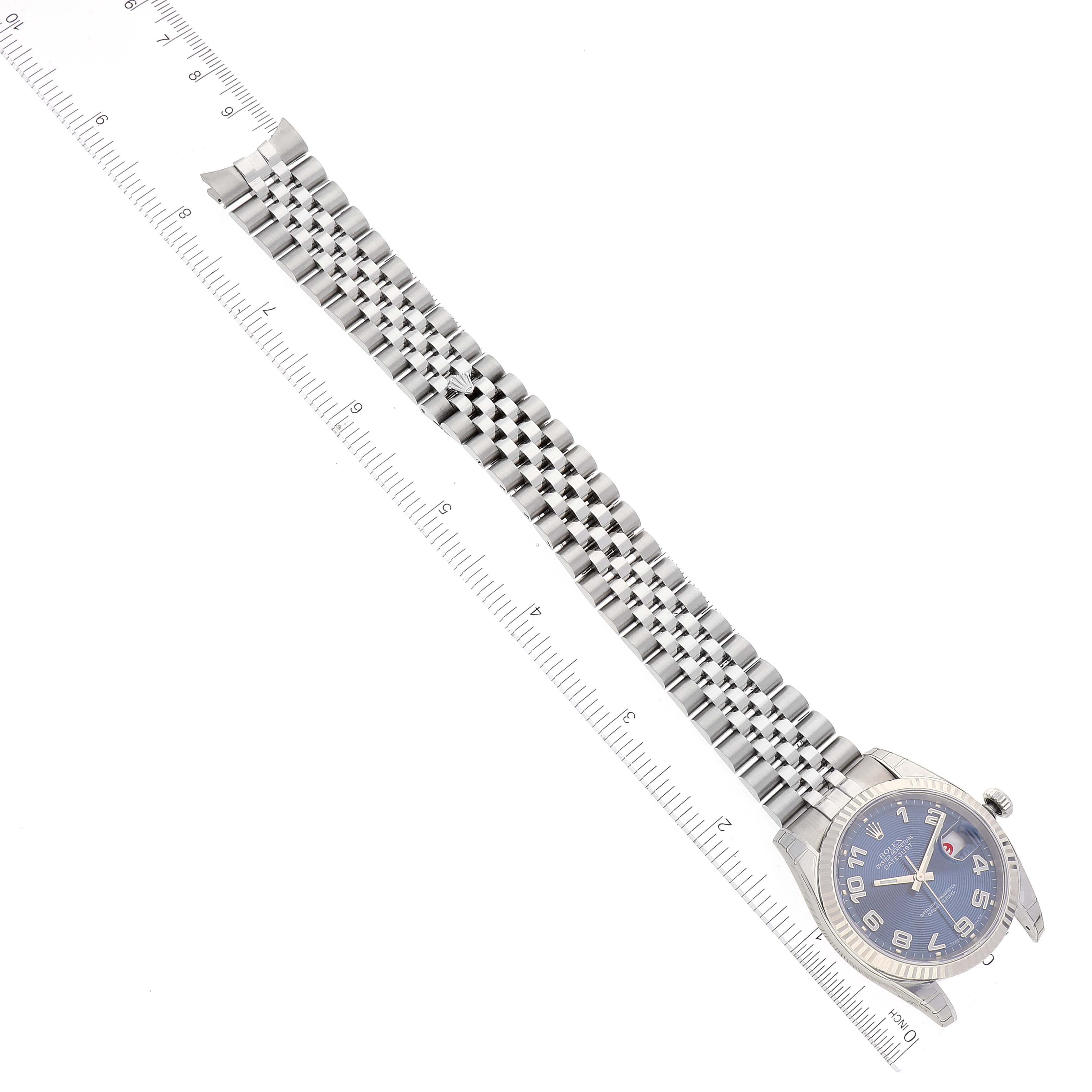 The image shows a top view of a Rolex Datejust 116234 Men's Stainless Steel Blue Dial 116234 Men's Stainless Steel Blue Dial watch and its metal bracelet alongside a ruler for scale.