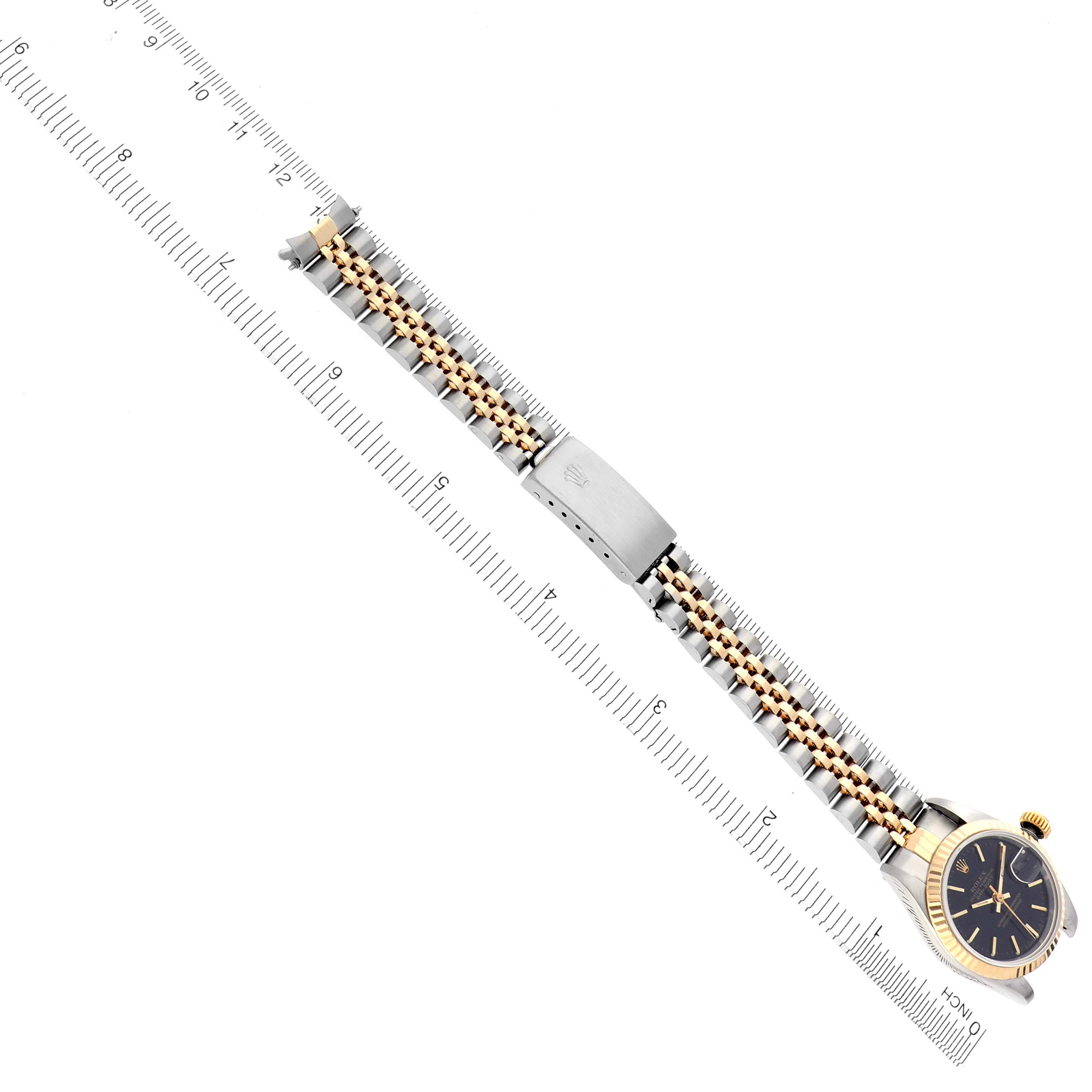 The Rolex Datejust 69173 Women's Steel and Gold (two tone) Black Dial 69173 Women's Steel and Gold (two tone) Black Dial is shown from a top-down angle, highlighting the watch face, bracelet, and clasp with a ruler for scale.