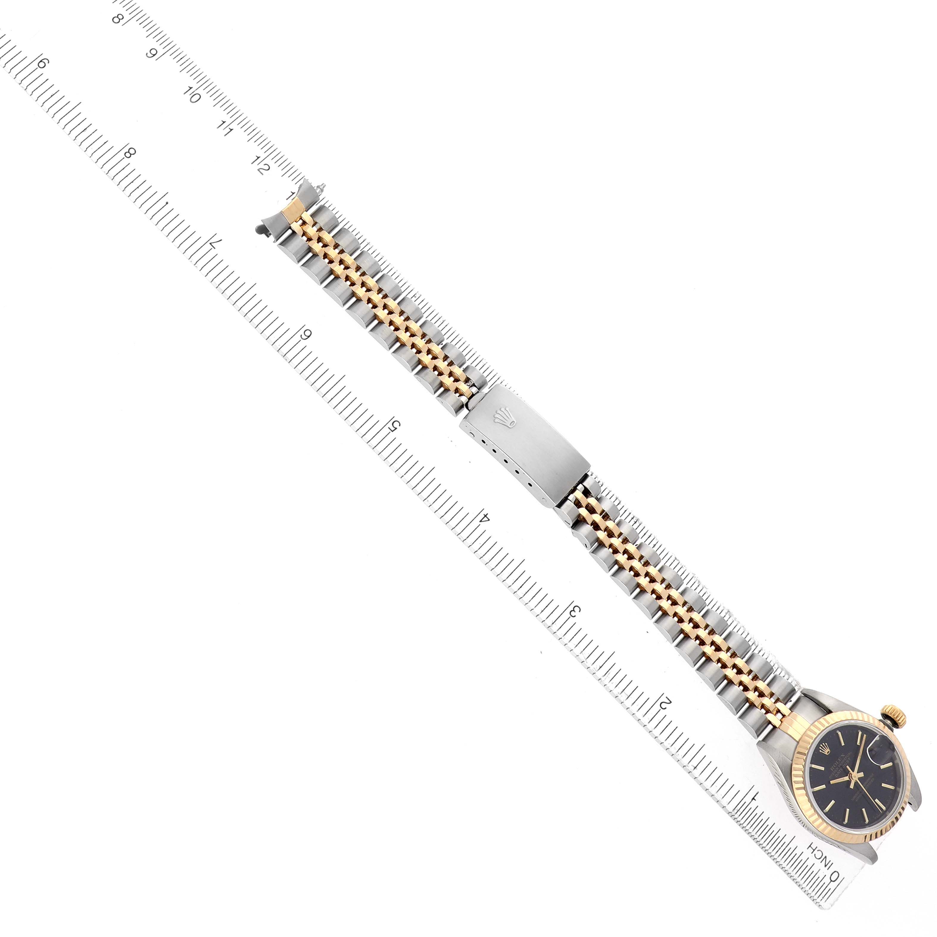 The Rolex Datejust 69173 Women's Steel and Gold (two tone) Black Dial is shown from a top-down angle, highlighting the watch face and full bracelet on a ruler.