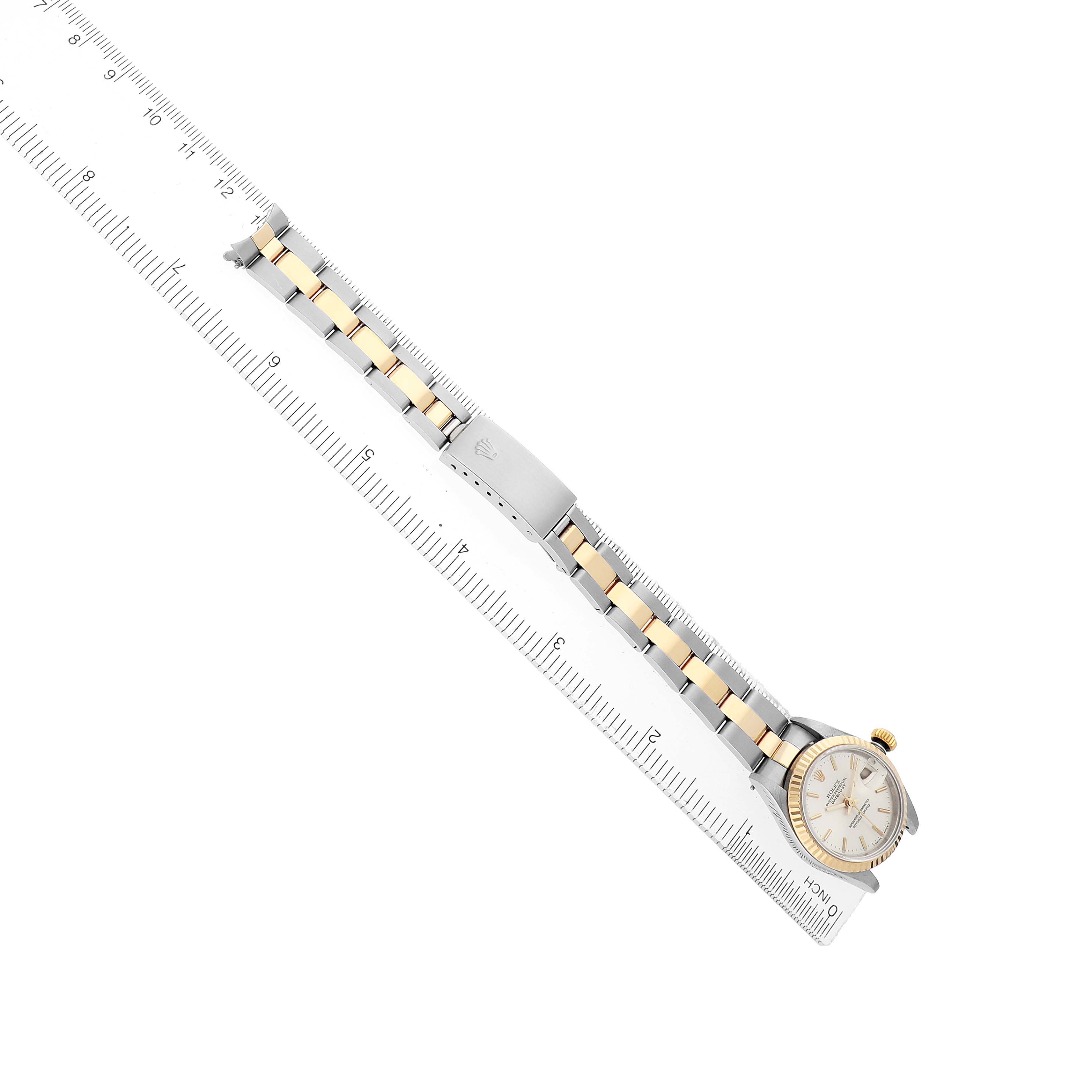The Rolex Datejust 79163 Women's Steel and Gold (two tone) Silver Dial watch is shown from a top-down angle, highlighting the band, clasp, and watch face alongside a ruler.