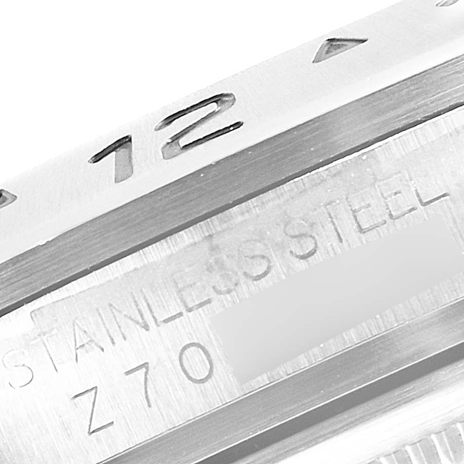The image shows a close-up of the bezel and part of the casing of a Rolex Explorer 16570 Men
s Stainless Steel Black Dial 16570 Men
s Stainless Steel Black Dial watch, highlighting the "12" marker and "Stainless Steel" engraving.