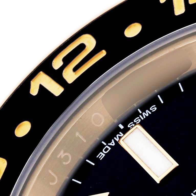 The image shows a close-up of the Rolex GMT-Master 116718LN Men's Yellow Gold Black Dial 116718LN Men's Yellow Gold Black Dial bezel and part of the dial, highlighting the 12-hour marker.