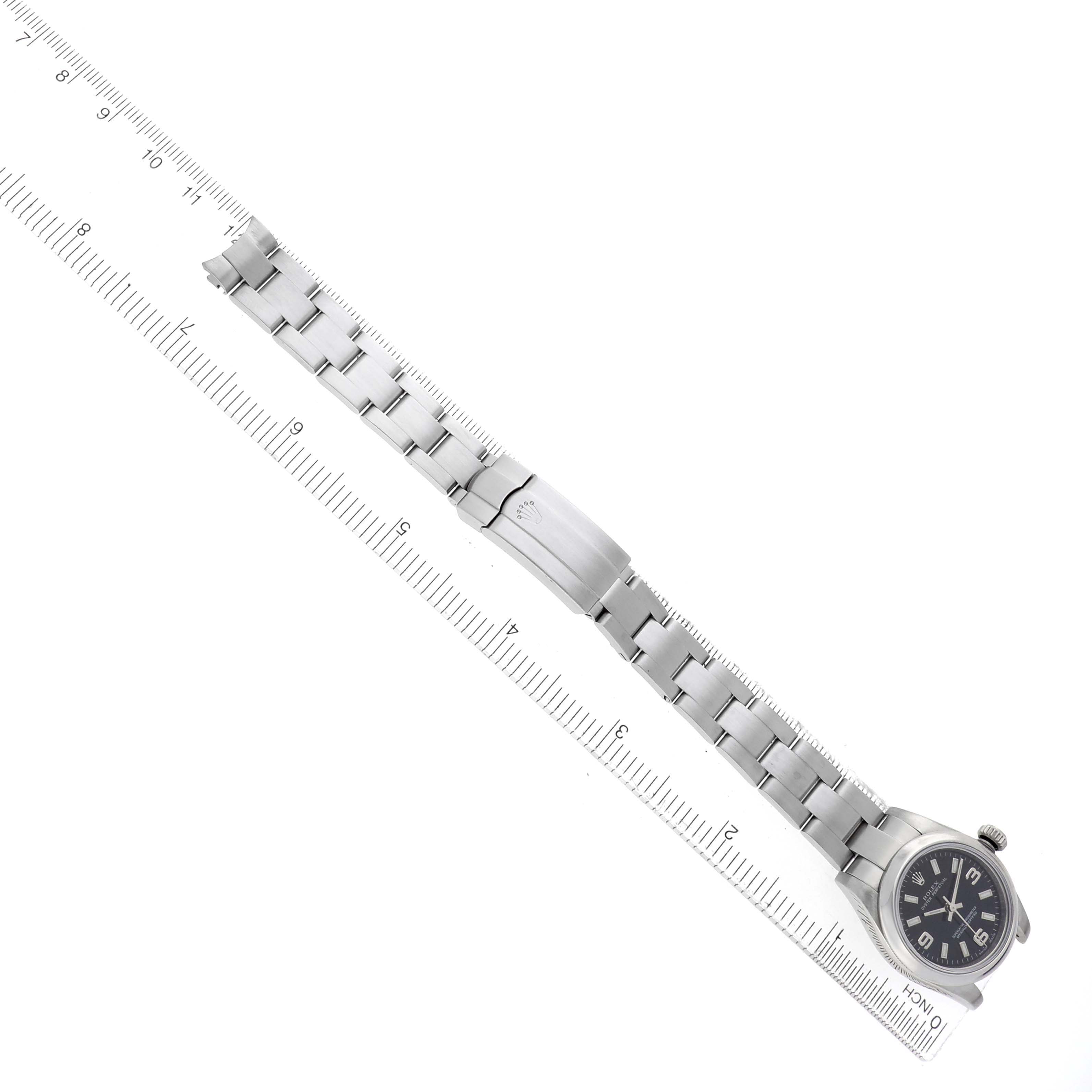 The Rolex Oyster Perpetual 176200 Women's Stainless Steel Black Dial watch is shown from an elevated angle, displaying the full bracelet and face alongside a ruler.