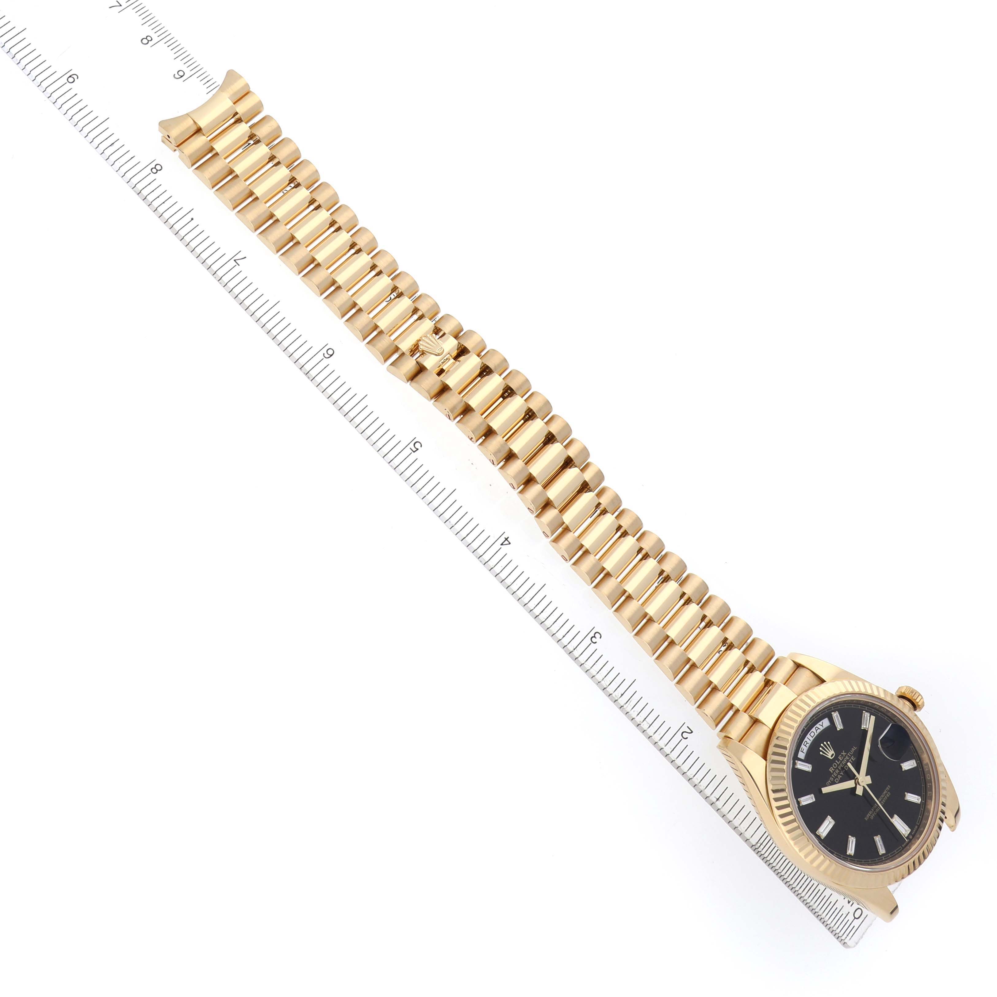 The Rolex President 228238 Men's Yellow Gold Black Dial watch is shown from a top angle, displaying its gold bracelet and black dial next to a ruler.