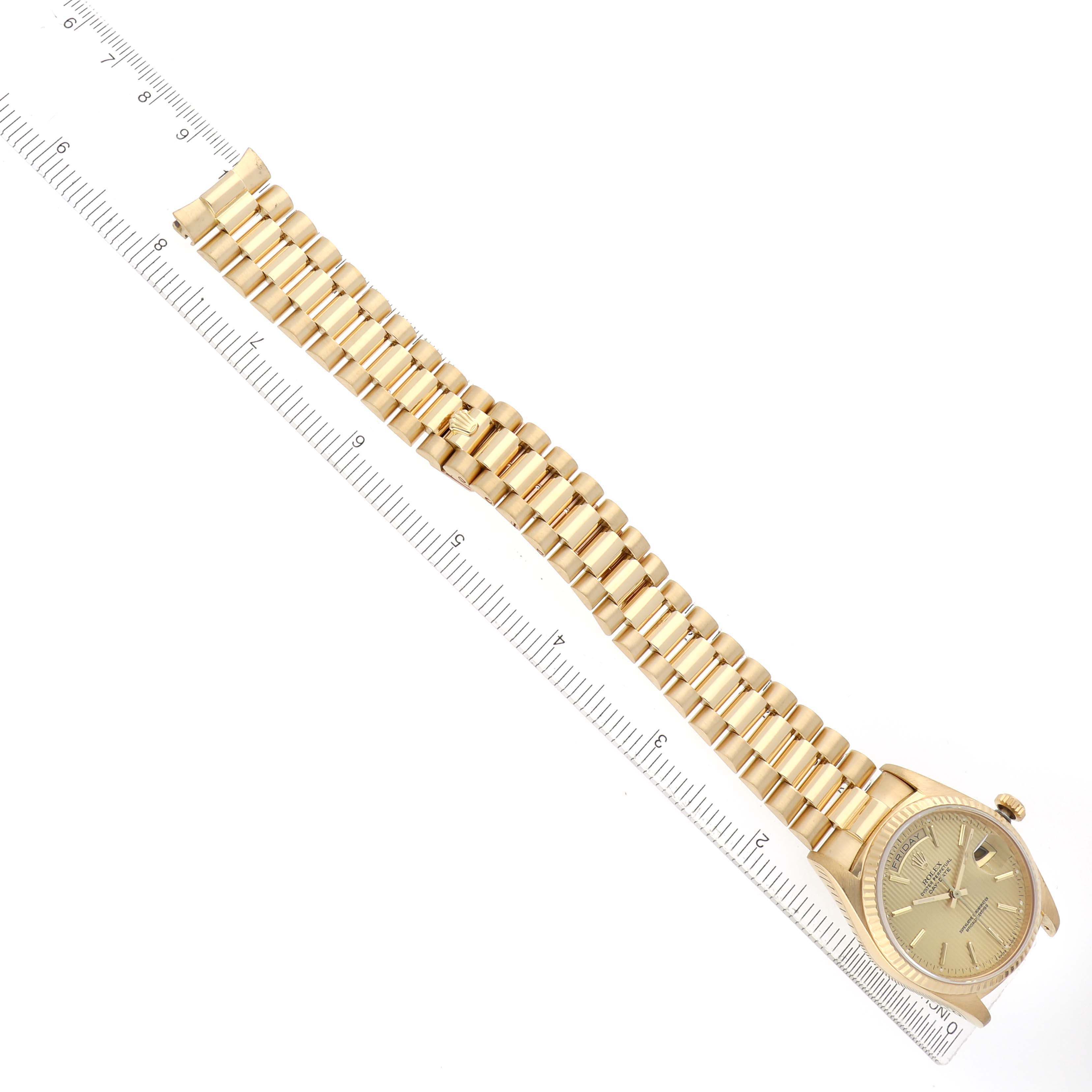 The Rolex President 18038 Men's Yellow Gold Champagne Dial model watch is shown in a top-down view, highlighting its gold band and face alongside a ruler.