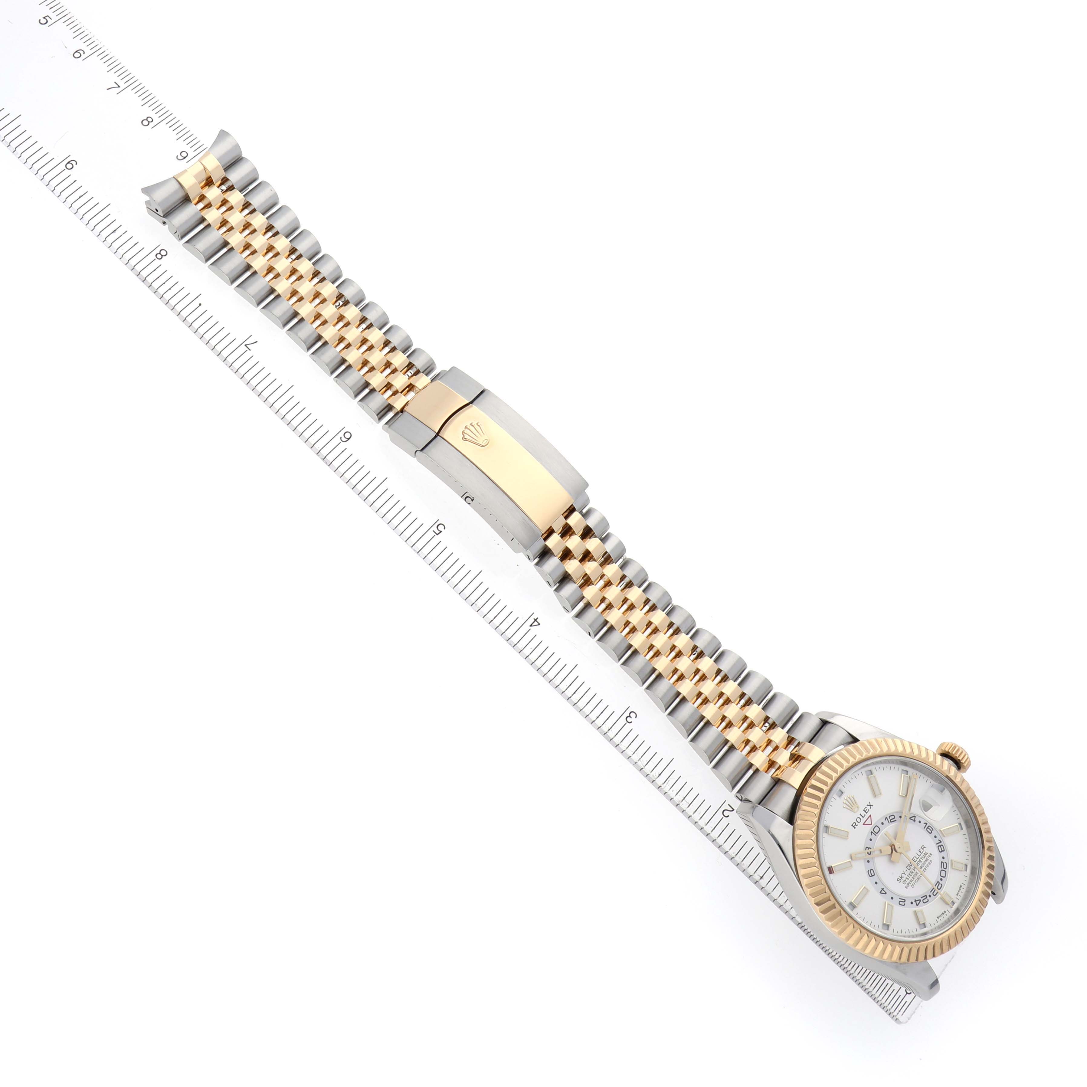 The image shows a Rolex Sky-Dweller 326933 Men's Steel and Gold (two tone) White Dial watch laid flat, displaying its bracelet, clasp, and partial face next to a ruler.