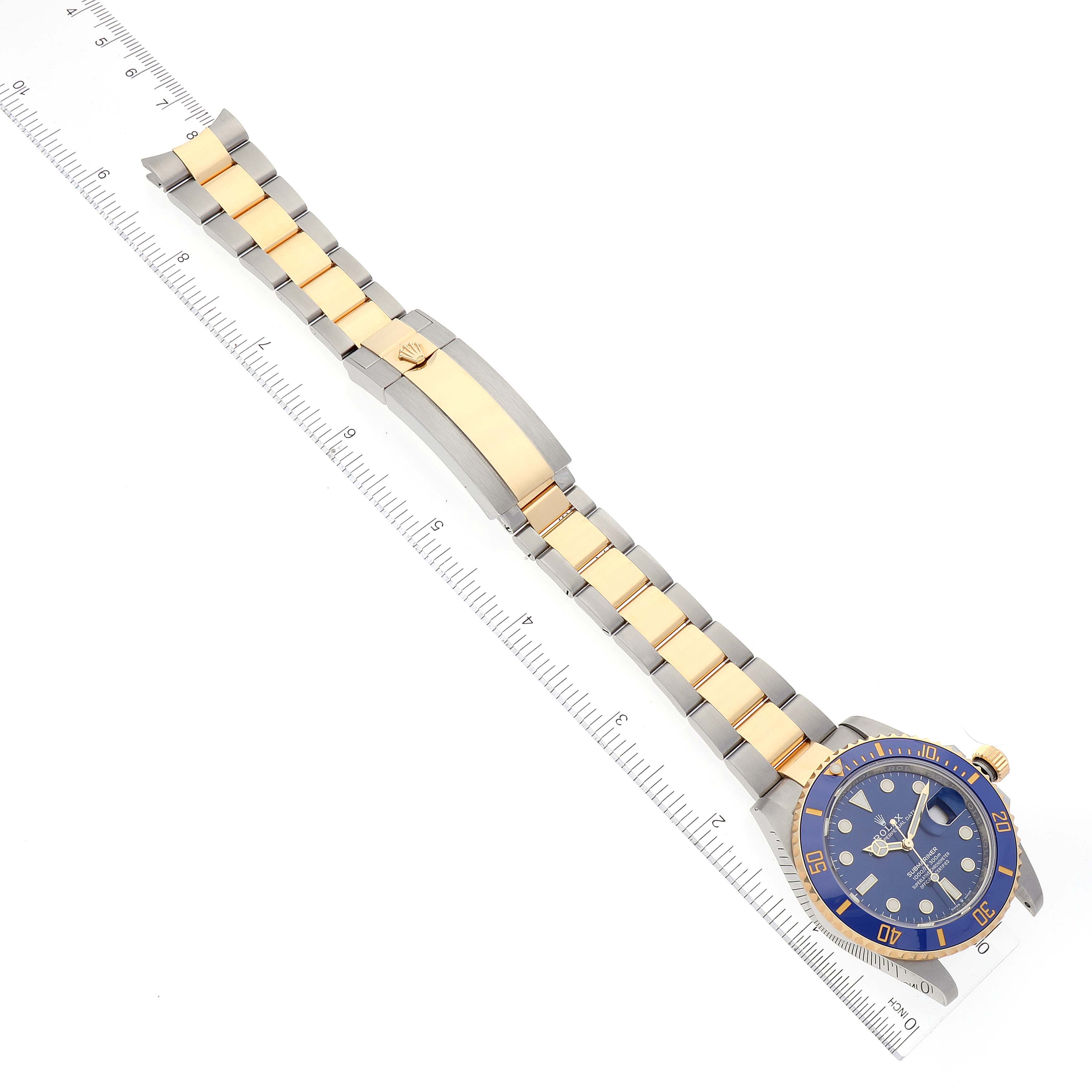 This image shows a Rolex Submariner 126613 Men's Steel and Gold (two tone) Blue Dial 126613 Men's Steel and Gold (two tone) Blue Dial watch laid flat with the band fully extended and positioned next to a ruler for scale.