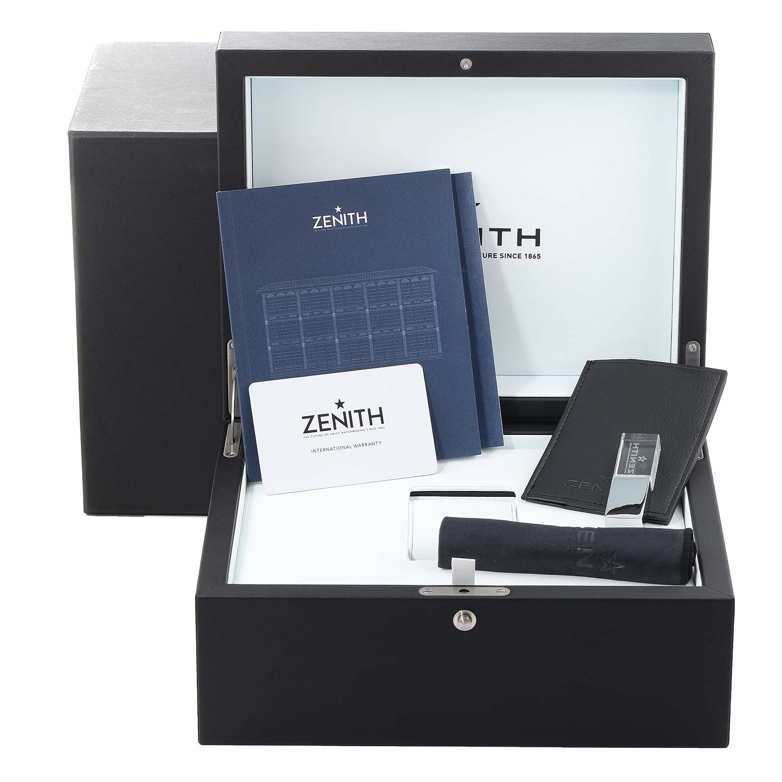 The image shows a Zenith Chronomaster 03.3100.3600 Men's Stainless Steel White Dial 03.3100.3600 Men's Stainless Steel White Dial watch box containing manuals, a warranty card, a strap tool, and a cleaning cloth.