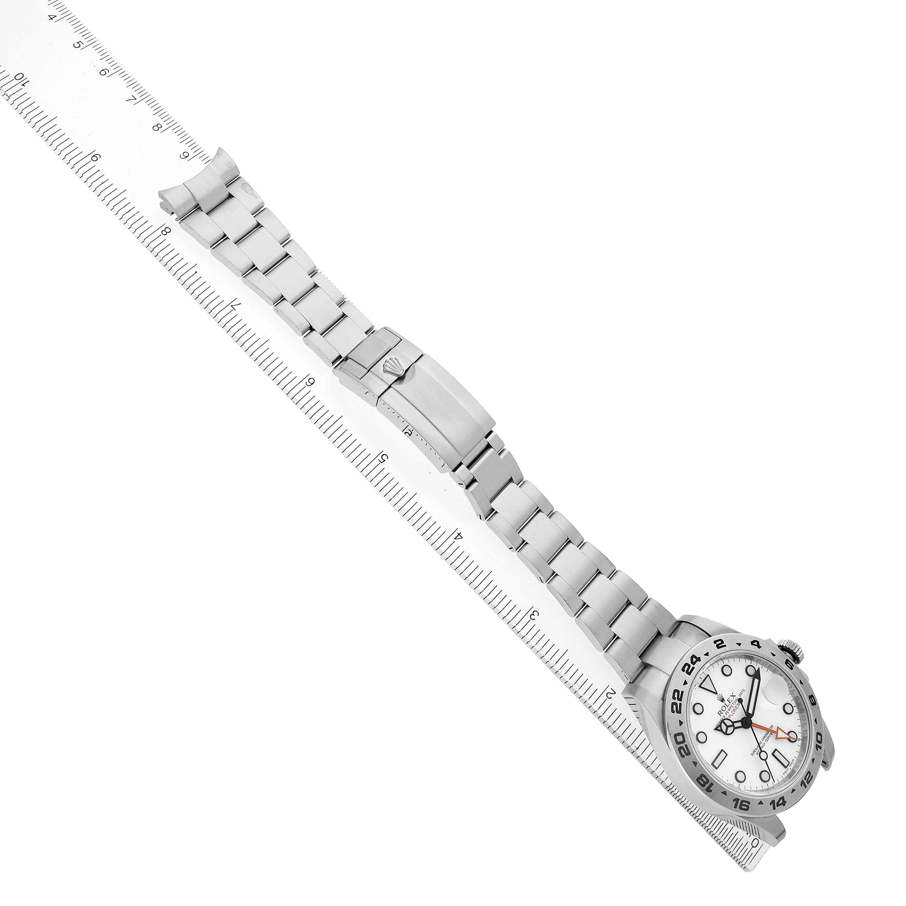 The Rolex Explorer 216570 Men's Stainless Steel White Dial watch is displayed diagonally, showing the full bracelet, case, and clasp alongside a ruler for scale.