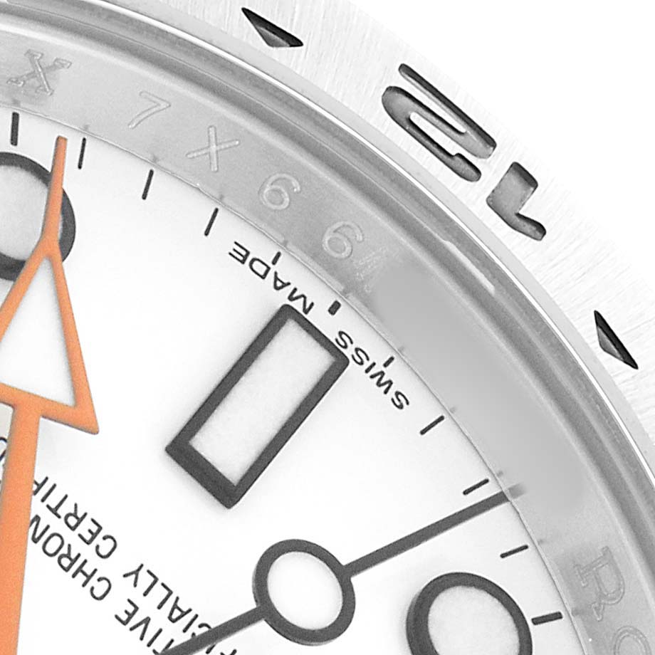 The image shows a partial close-up of the Rolex Explorer 216570 Men's Stainless Steel White Dial's bezel and dial, highlighting the hour markers and orange hand.