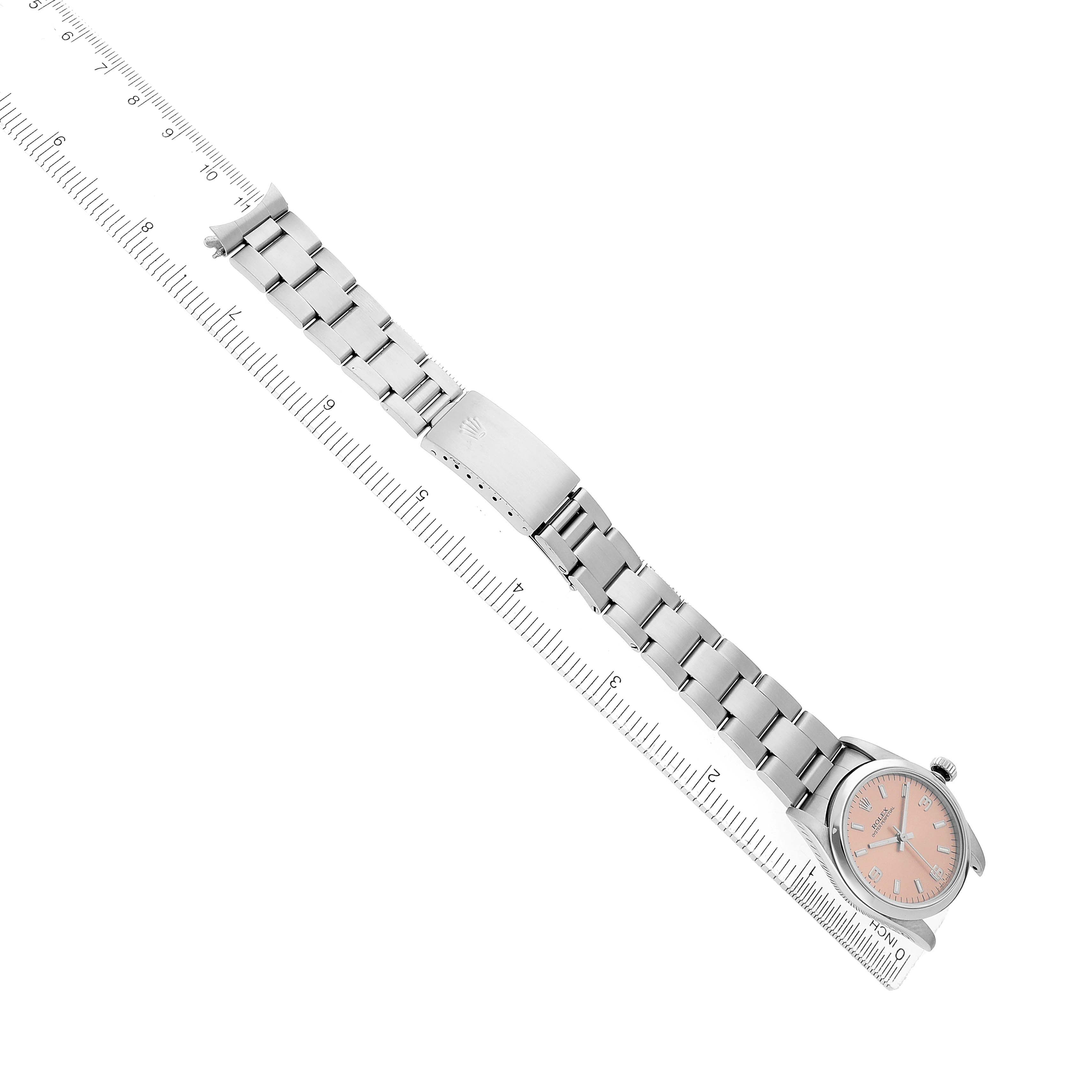 The Rolex Mid-Size 67480 Women's Stainless Steel Pink Dial watch is shown at a diagonal angle, displaying the bracelet, clasp, and face with a pink dial.