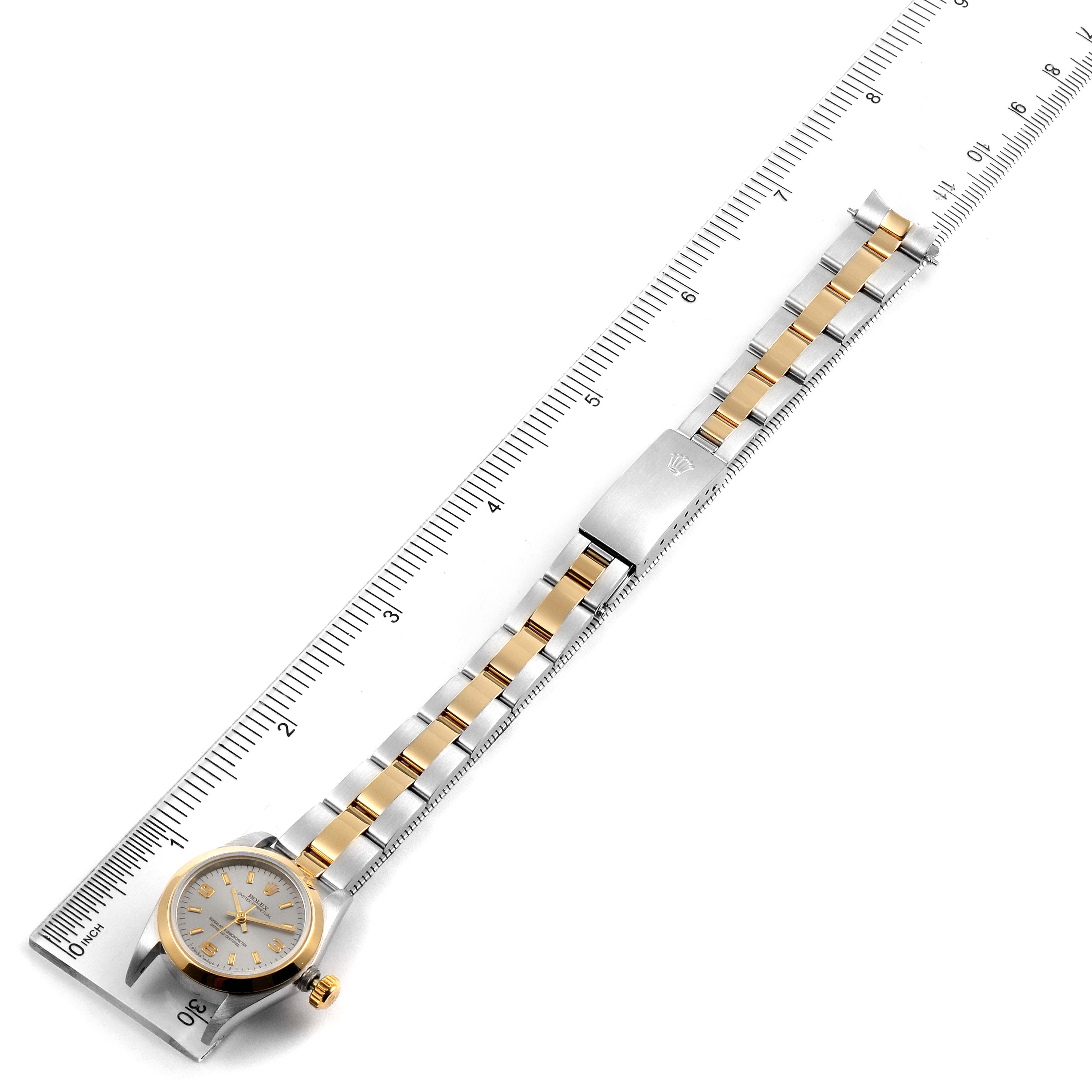 This image shows a Rolex Oyster Perpetual 76193 Women's Steel and Gold (two tone) Grey Dial 76193 Women's Steel and Gold (two tone) Grey Dial watch laid flat along a ruler, displaying its face and gold-and-silver bracelet.