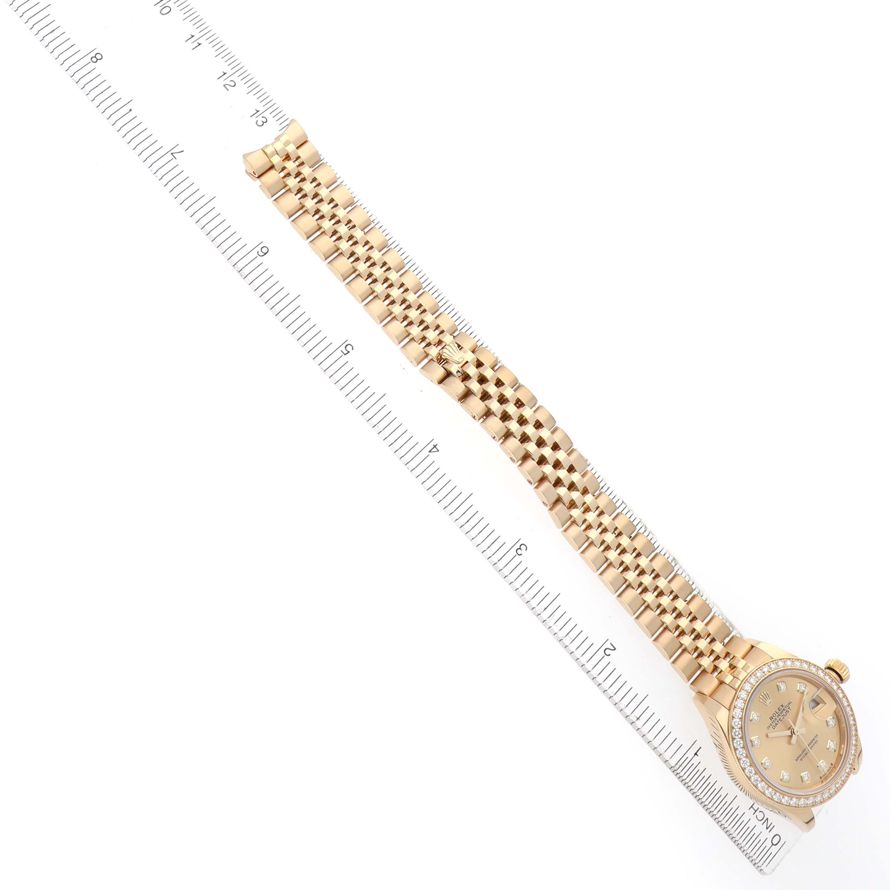 The Rolex President 279138 Women's Yellow Gold Champagne Dial watch is shown from a top view, displaying its face, bezel, and bracelet beside a measuring ruler.