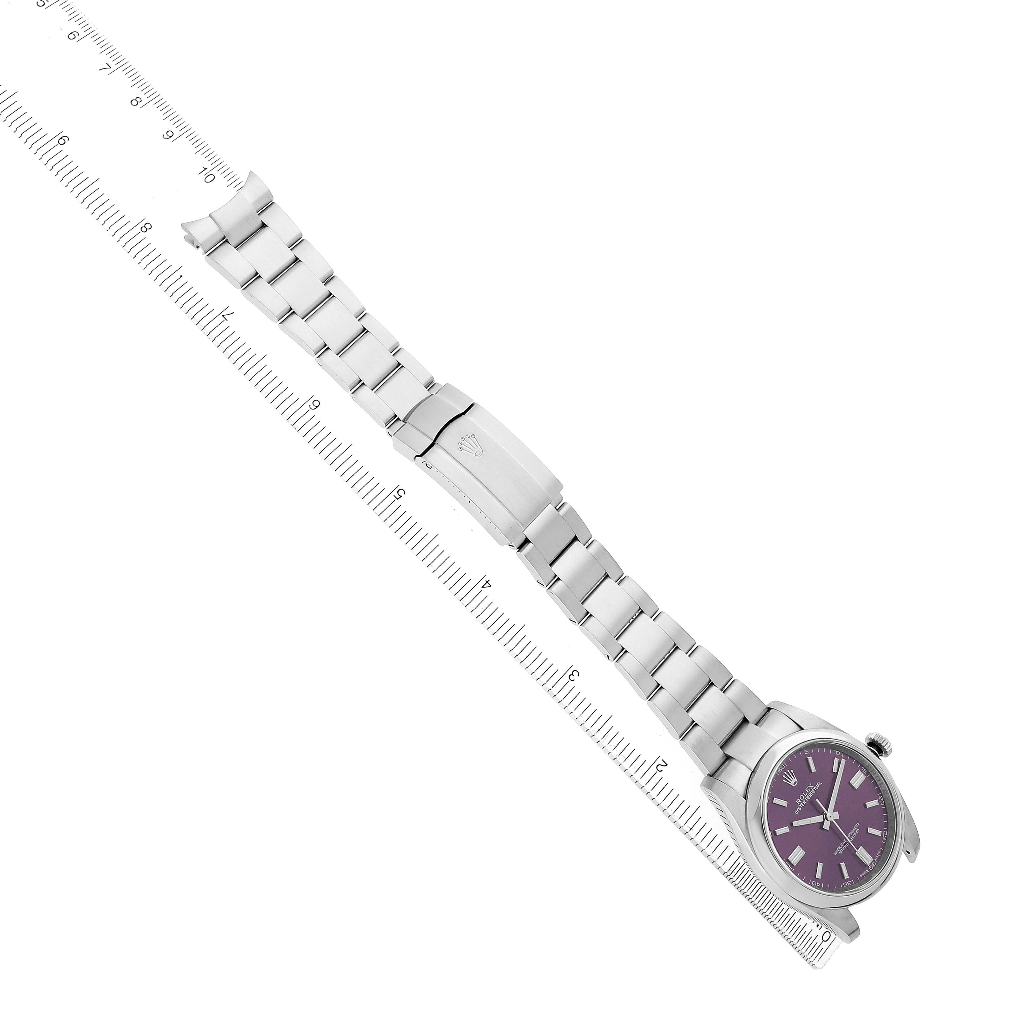 The image displays a Rolex Oyster Perpetual 116000 Men's Stainless Steel Purple Dial watch with a purple dial, angled diagonally with the bracelet fully extended alongside a ruler.
