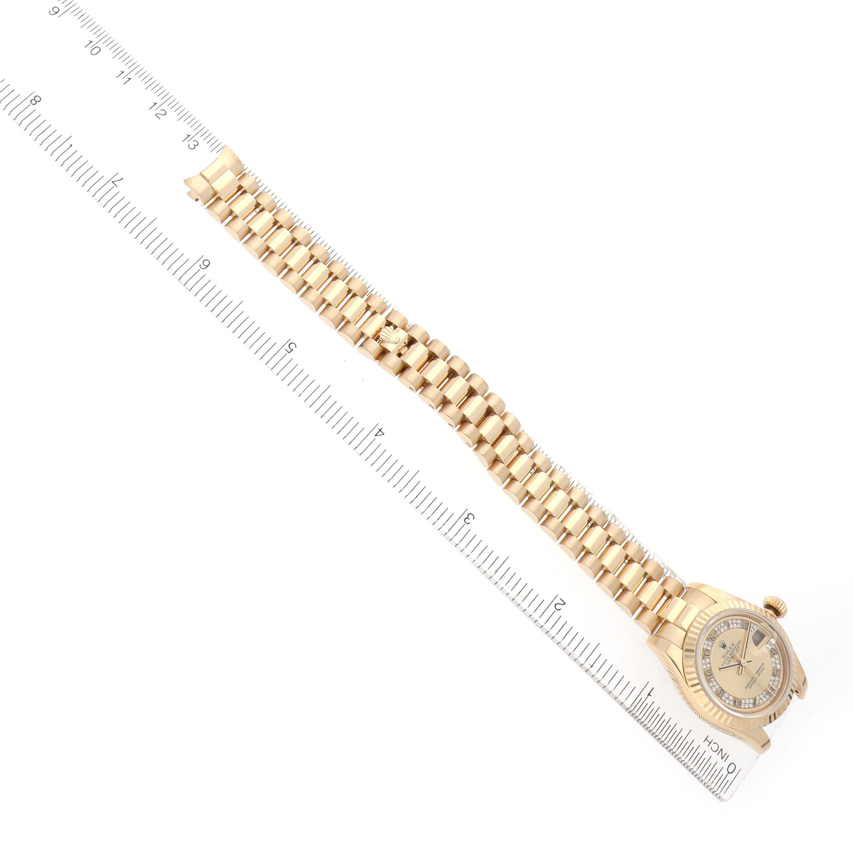 The Rolex President 179178 Women's Yellow Gold Champagne Dial model is shown from a top view, highlighting the watch face and full bracelet beside a ruler.