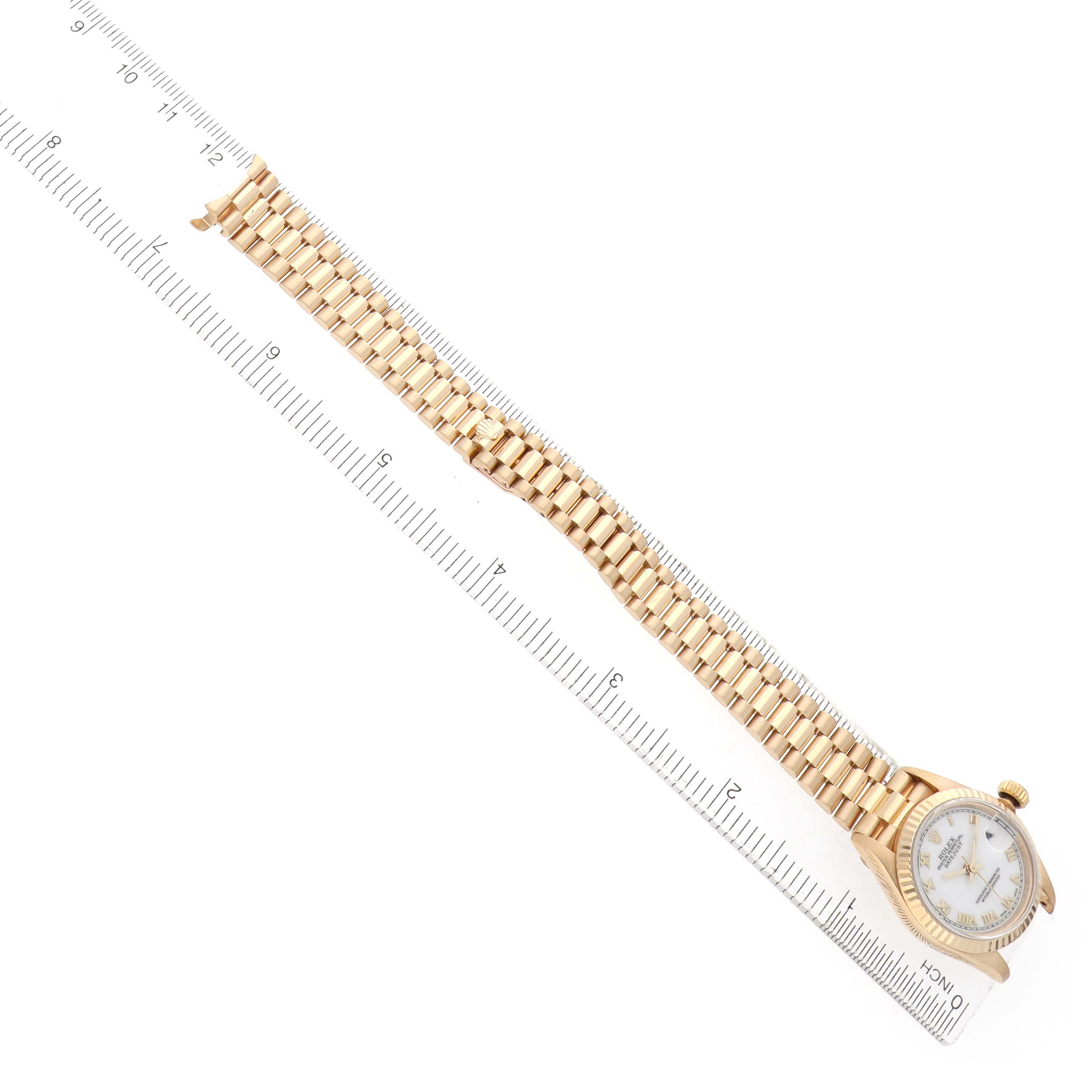 The Rolex President 69178 Women's Yellow Gold White Dial watch is shown from a top-down angle, displaying its bracelet and dial alongside a ruler.