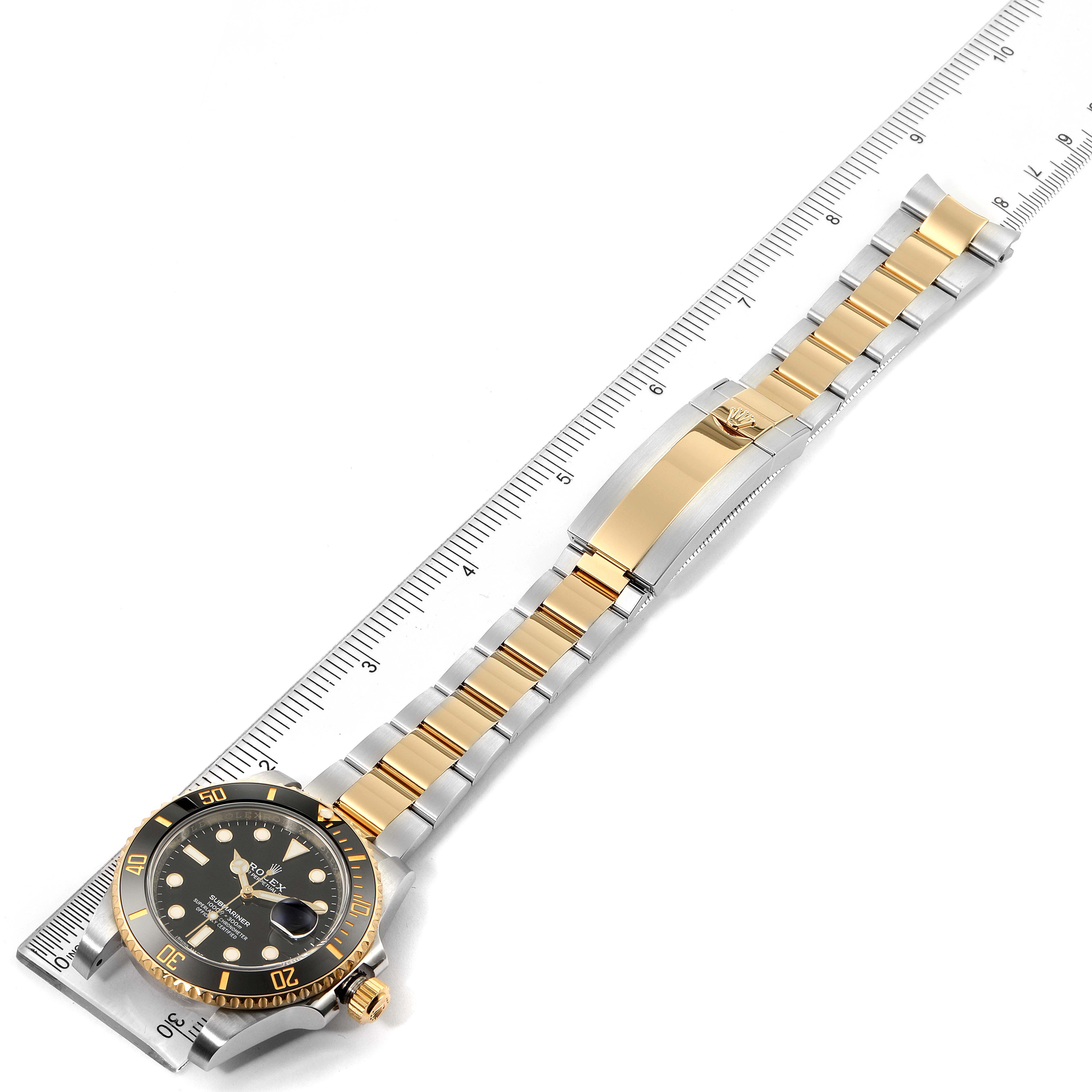 The Rolex Submariner 116613 Men's Steel and Gold (two tone) Black Dial 116613 Men's Steel and Gold (two tone) Black Dial watch is shown from a top-down angle, highlighting its face, bezel, and two-tone bracelet with a ruler for scale.