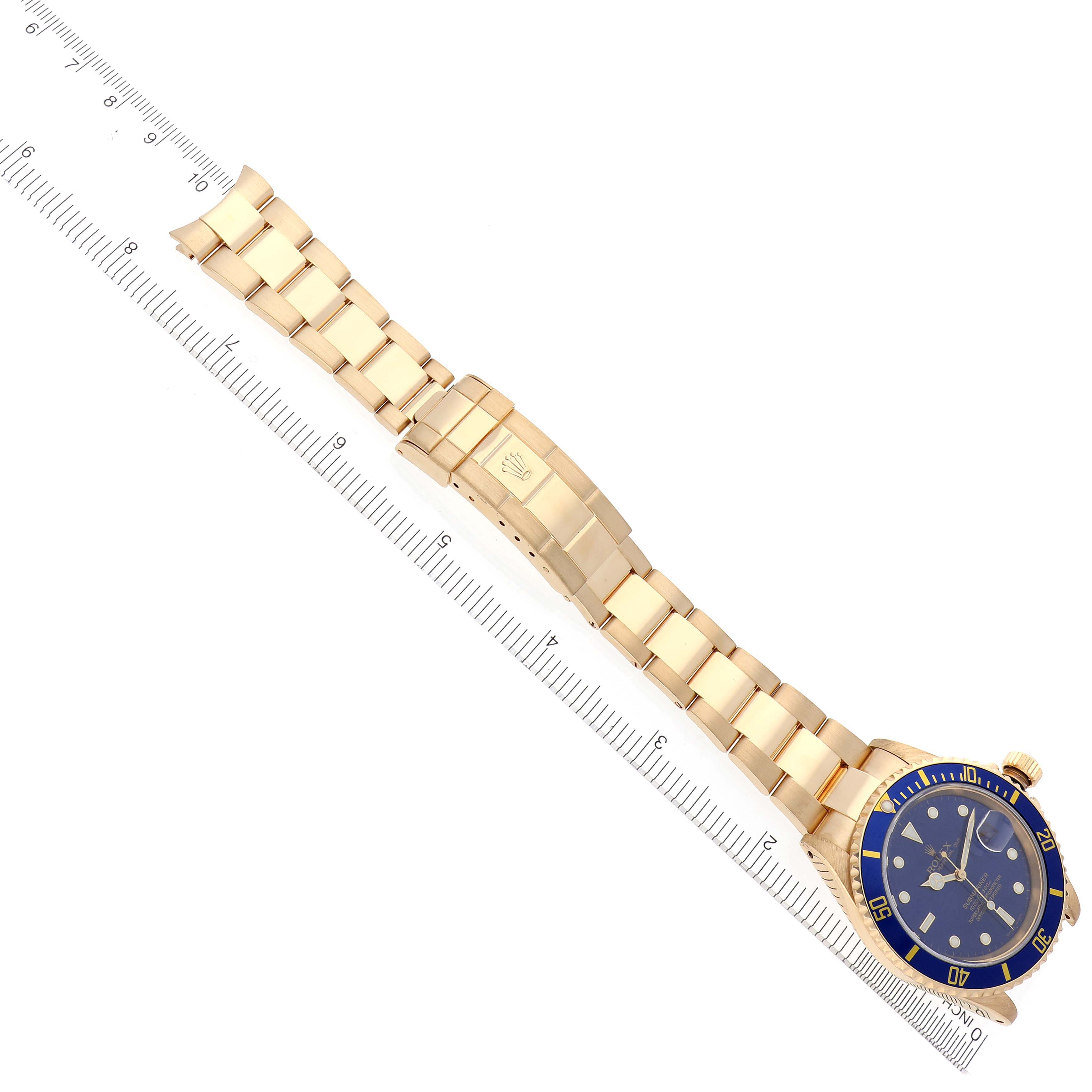 The Rolex Submariner 16618 Men's Yellow Gold Blue Dial 16618 Men's Yellow Gold Blue Dial watch is shown at a diagonal angle, displaying its blue bezel and gold bracelet with a ruler for scale.
