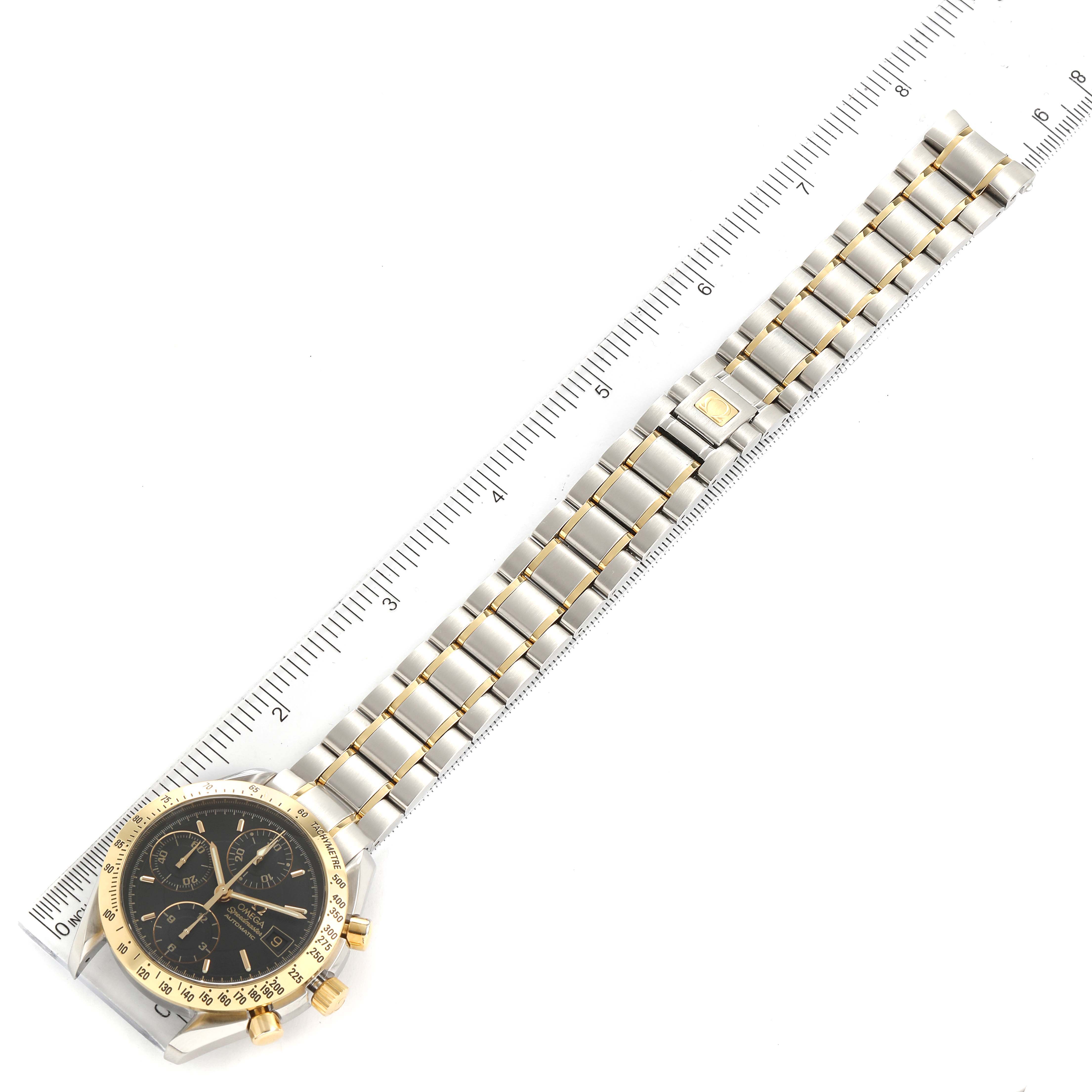 This image shows the Omega Speedmaster 3313.50.00 Men's Steel and Gold (two tone) Black Dial 3313.50.00 Men's Steel and Gold (two tone) Black Dial watch laid flat with a ruler for scale, displaying the face, bracelet, and clasp.