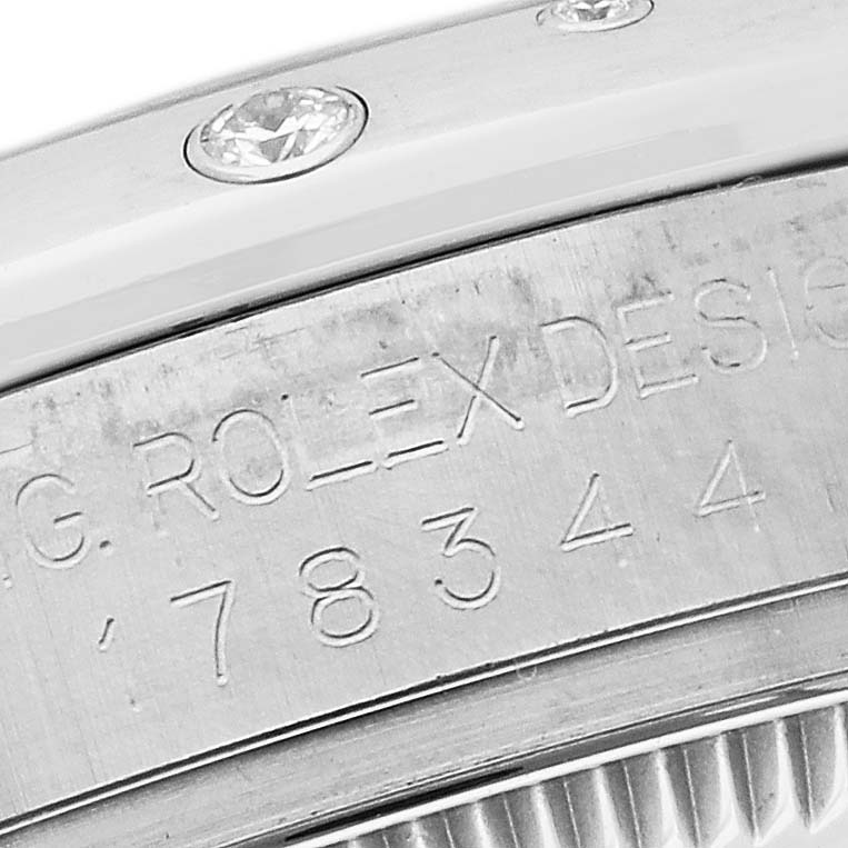 The image shows a close-up of the side of a Rolex Mid-Size 178344 Women's Stainless Steel Silver Dial 178344 Women's Stainless Steel Silver Dial watch case, highlighting the engraving and gemstones.