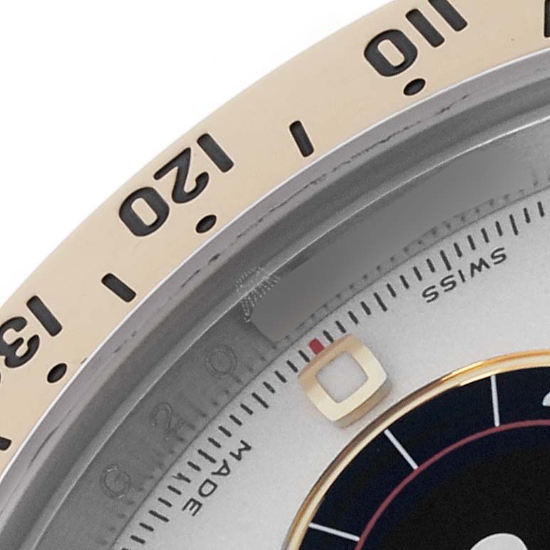 The image shows a close-up of the bezel and dial of a Rolex Daytona 116523 Men's Steel and Gold (two tone) Silver Dial 116523 Men's Steel and Gold (two tone) Silver Dial, focusing on the 12 to 13 section.