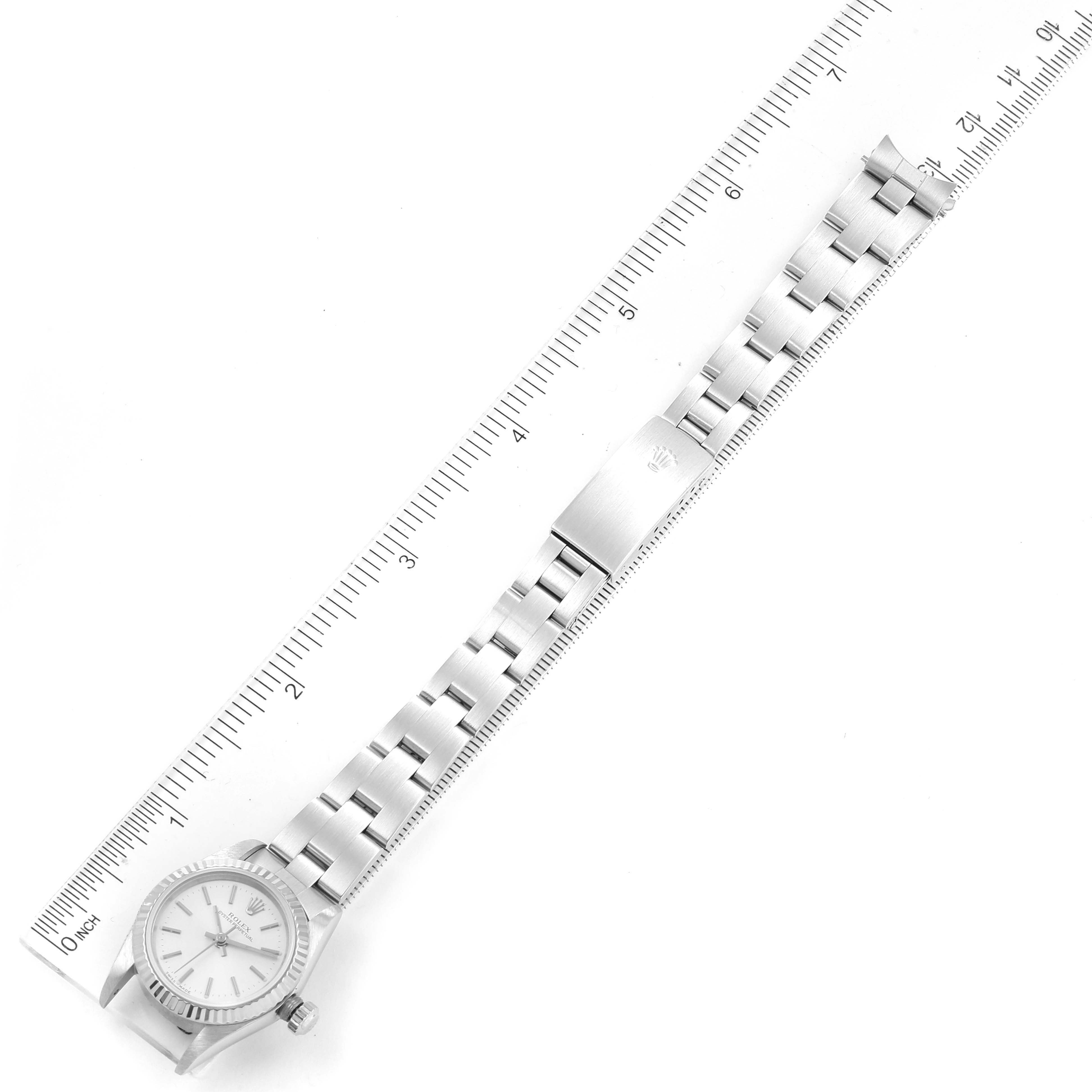 The image shows a top-down view of a Rolex Oyster Perpetual 76094 Women's Stainless Steel Silver Dial 76094 Women's Stainless Steel Silver Dial watch with its bracelet fully extended alongside a ruler.