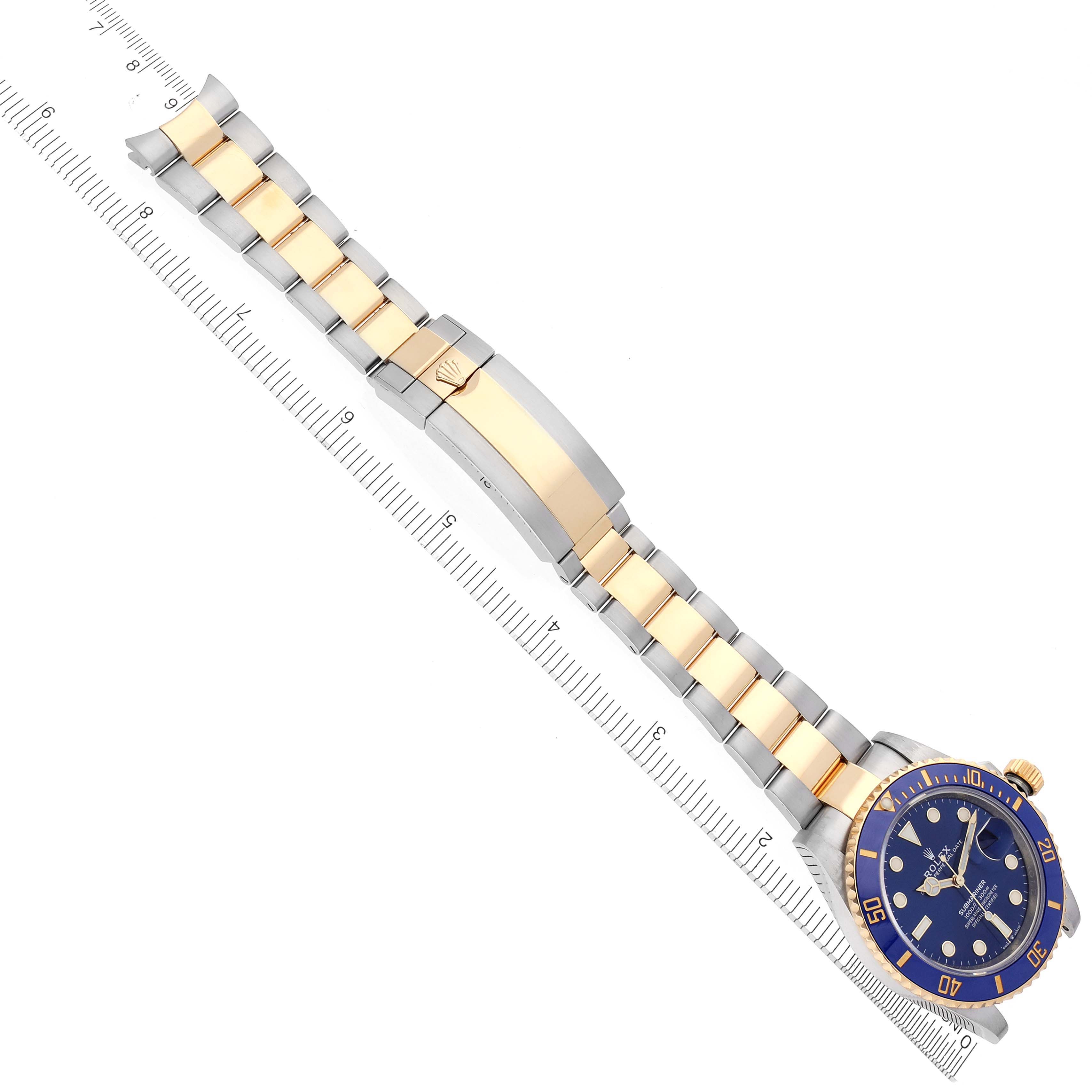 The image shows a Rolex Submariner 126613 Men's Steel and Gold (two tone) Blue Dial 126613 Men's Steel and Gold (two tone) Blue Dial watch laid flat, displaying the bracelet, clasp, and blue bezel with a ruler beside it.