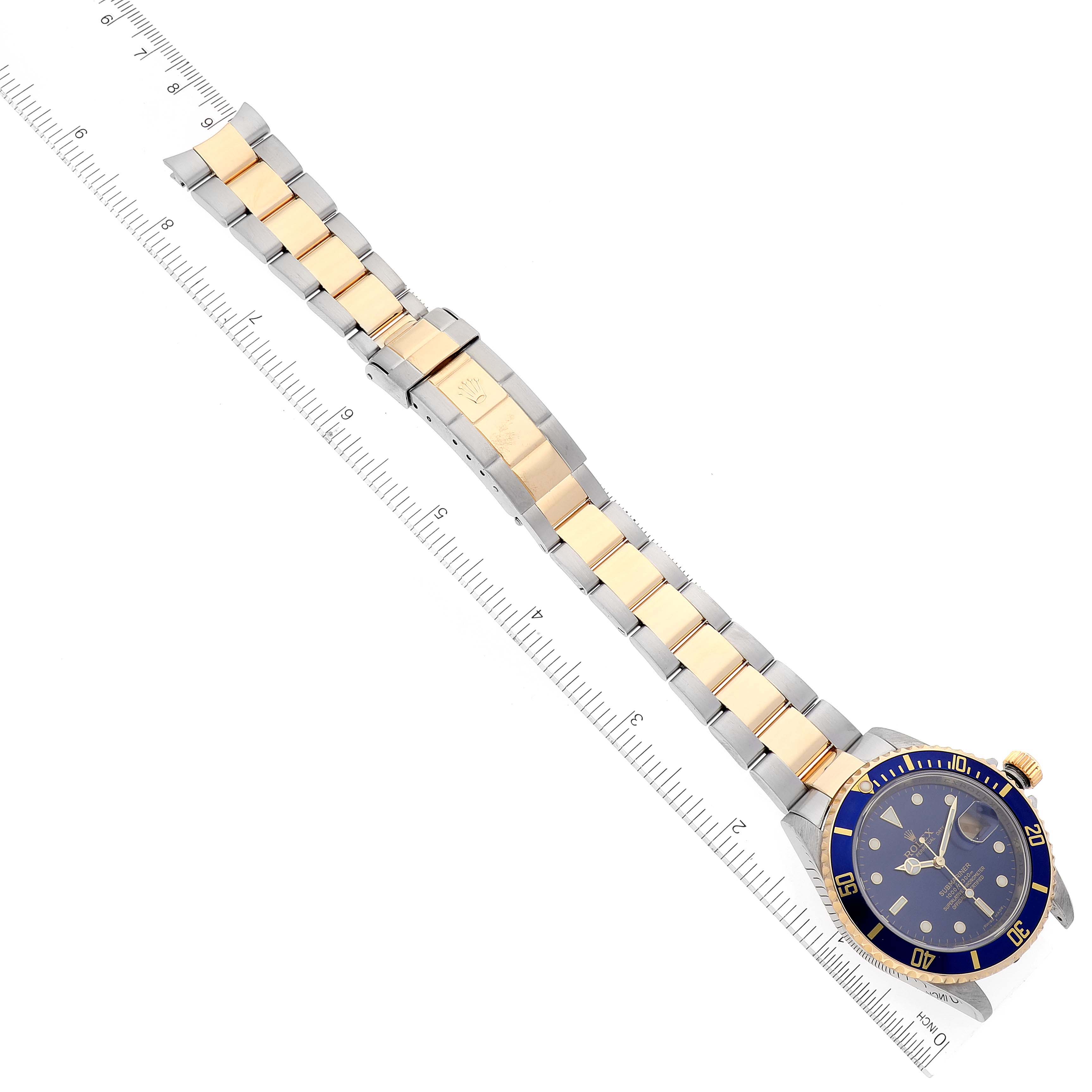 The image shows a top view of a Rolex Submariner 16613 Men's Steel and Gold (two tone) Blue Dial 16613 Men's Steel and Gold (two tone) Blue Dial watch, including its bezel, dial, and bracelet beside a ruler.