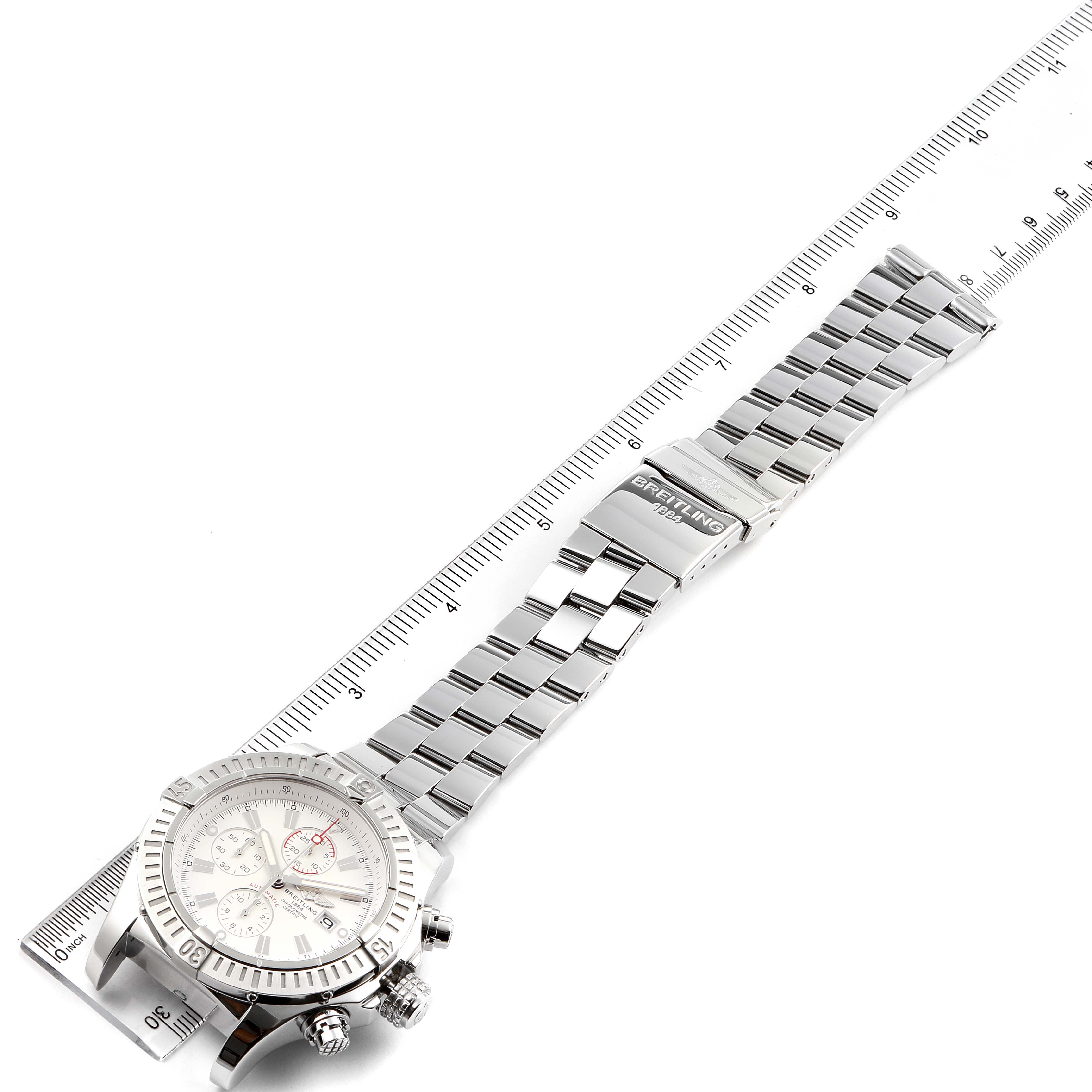 The image shows a top-down view of a Breitling Avenger A13370 Men's Stainless Steel White Dial A13370 Men's Stainless Steel White Dial watch, featuring its face, bezel, and metal bracelet laid beside a ruler.