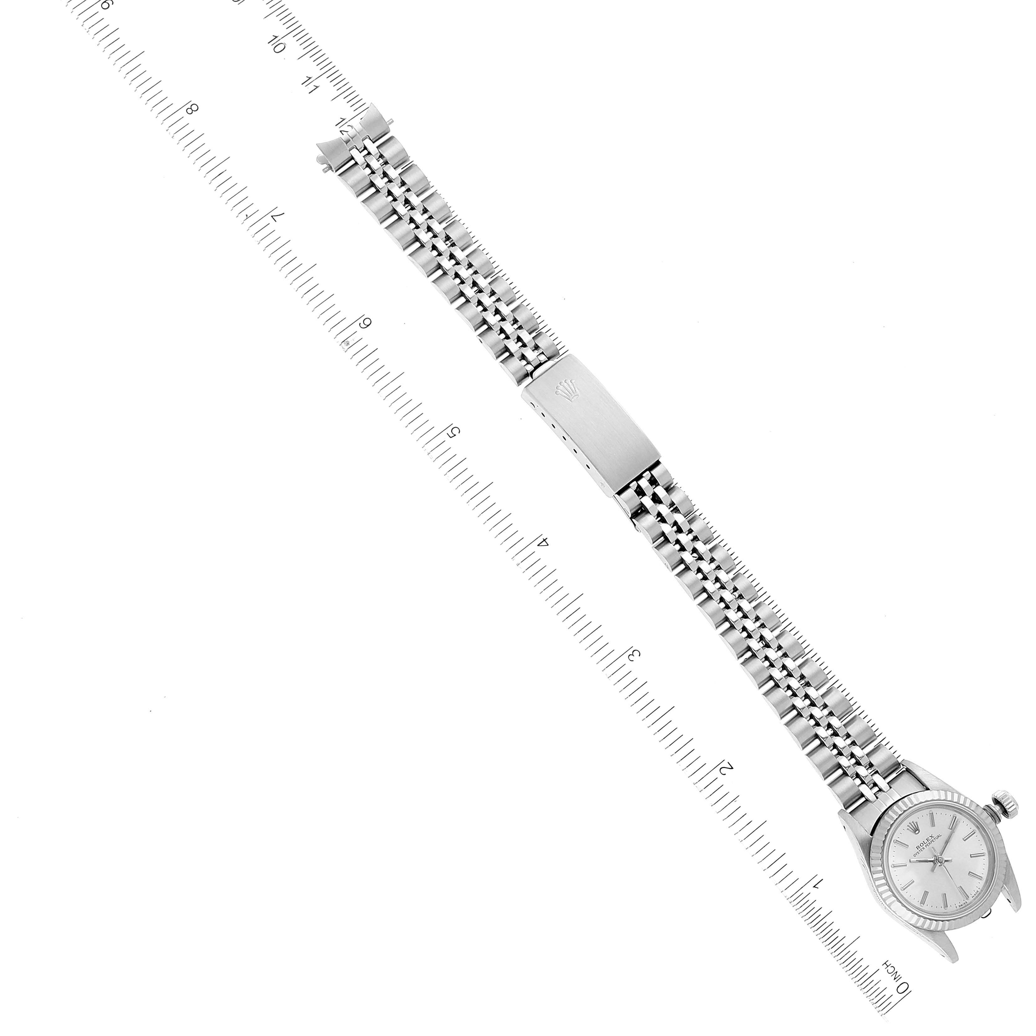 The image shows a top view of a Rolex Oyster Perpetual 67194 Women
s Stainless Steel Silver Dial 67194 Women
s Stainless Steel Silver Dial watch with its full bracelet extended alongside a ruler.