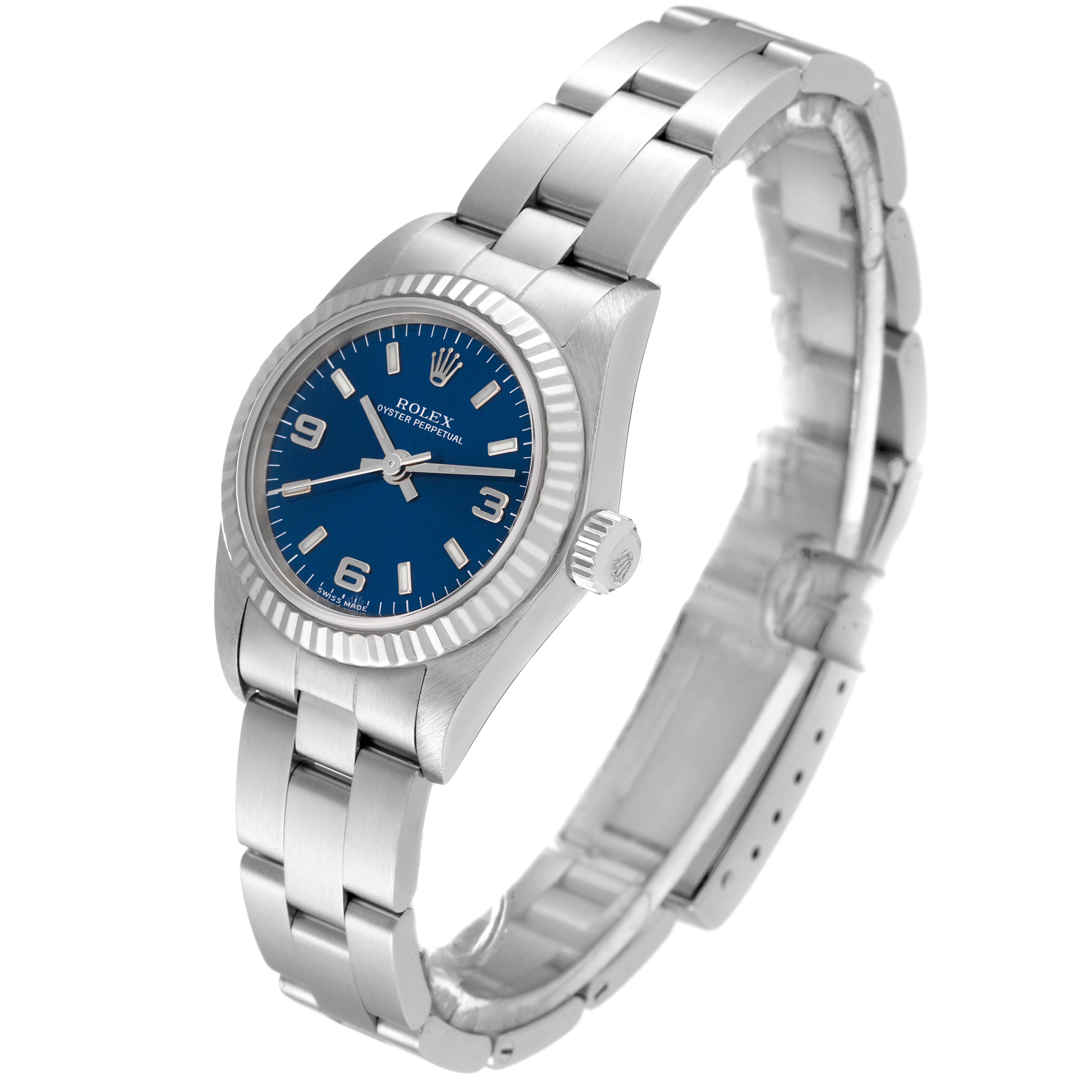 The image shows a side view of the Rolex Oyster Perpetual 76094 Women's Stainless Steel Blue Dial 76094 Women's Stainless Steel Blue Dial watch, highlighting its blue dial, fluted bezel, and metal bracelet.