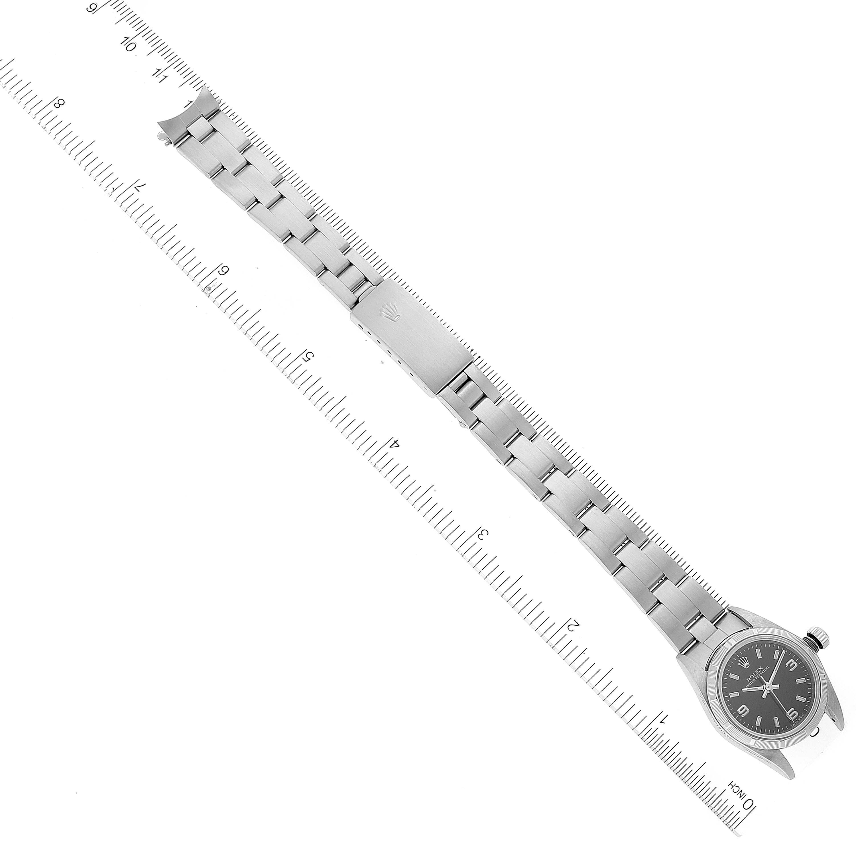 This image shows a Rolex Oyster Perpetual 76030 Women's Stainless Steel Black Dial 76030 Women's Stainless Steel Black Dial watch laid flat with the strap extended and a ruler for scale.