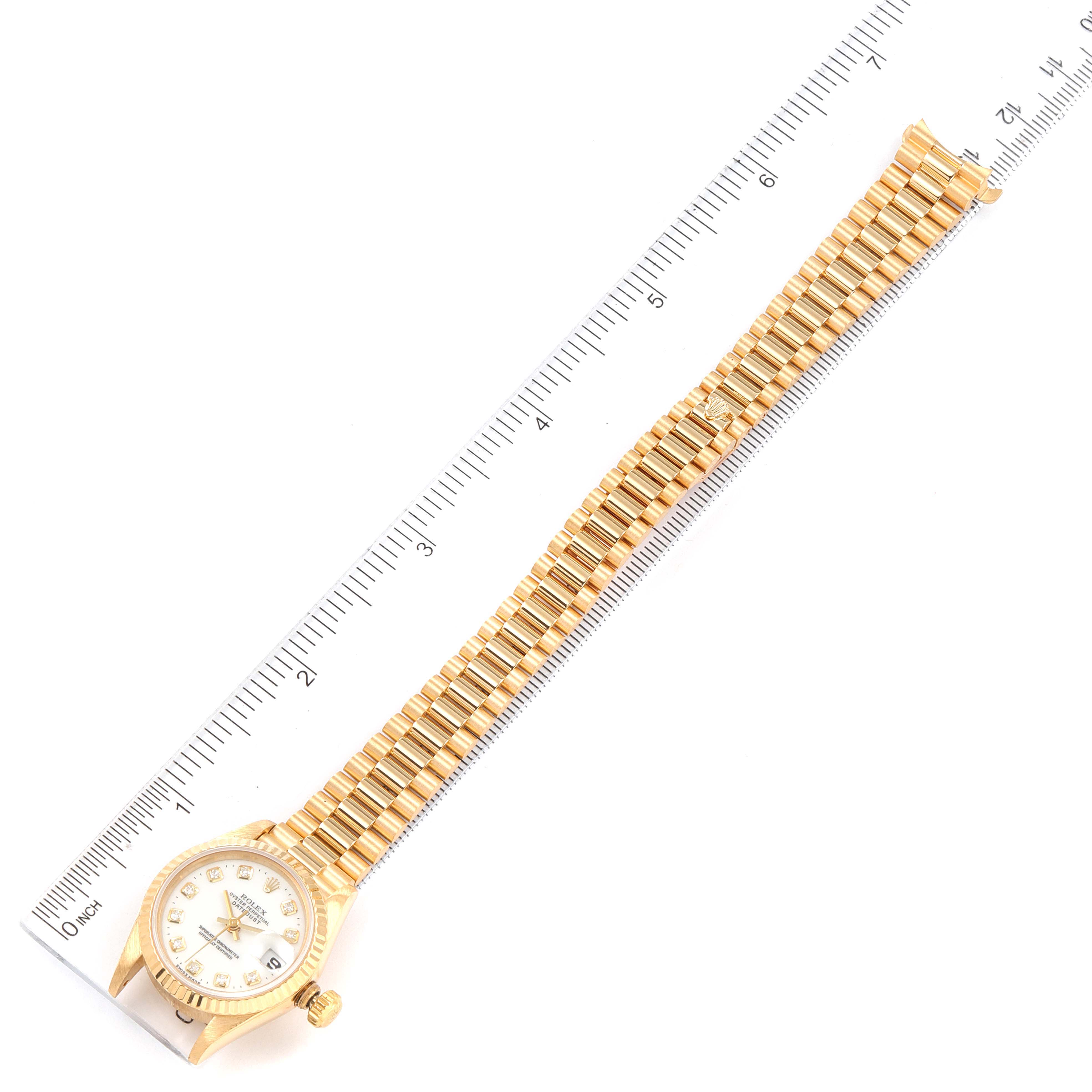 The image shows the front view of a Rolex President 69178 Women
s Yellow Gold White Dial 69178 Women
s Yellow Gold White Dial model watch next to a measuring scale.