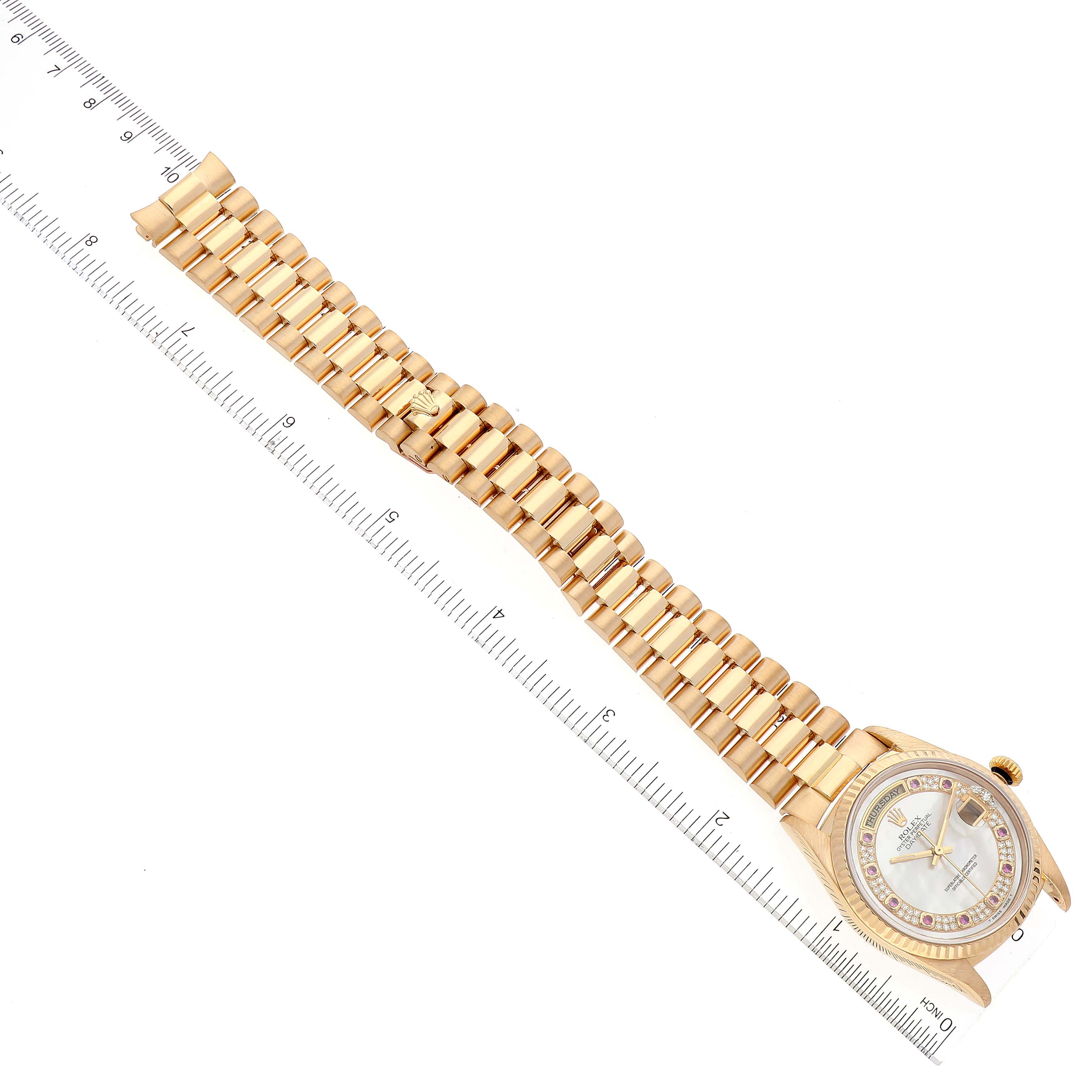 This image of a Rolex President 18238 Men's Yellow Gold Mother of Pearl Dial 18238 Men's Yellow Gold Mother of Pearl Dial model watch shows the face, bezel, crown, and entire bracelet laid next to a ruler.