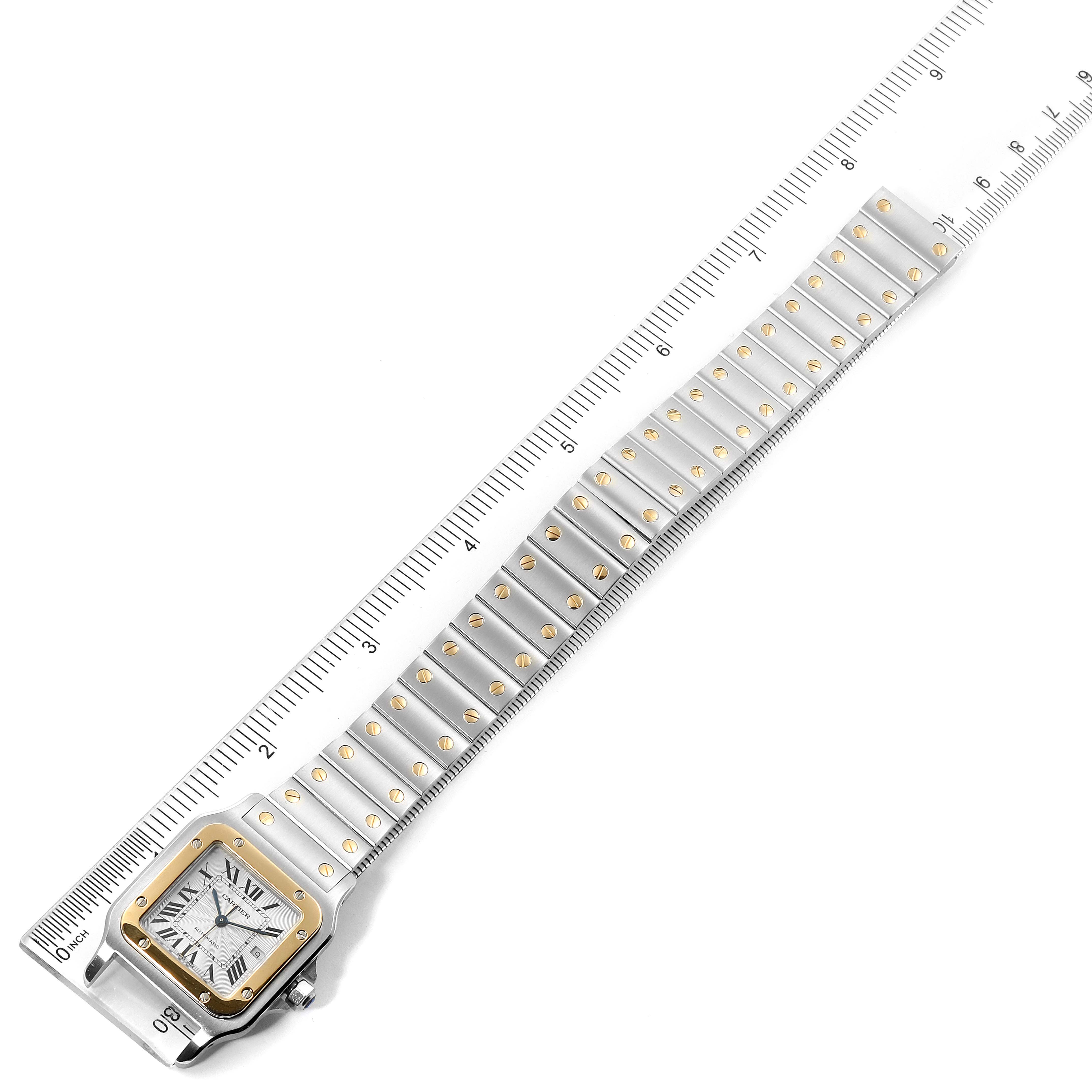 This image displays a Cartier Santos W20058C4 Men
s Steel and Gold (two tone) Silver Dial W20058C4 Men
s Steel and Gold (two tone) Silver Dial watch laid flat, showcasing the face and full length of the band with a ruler for scale.
