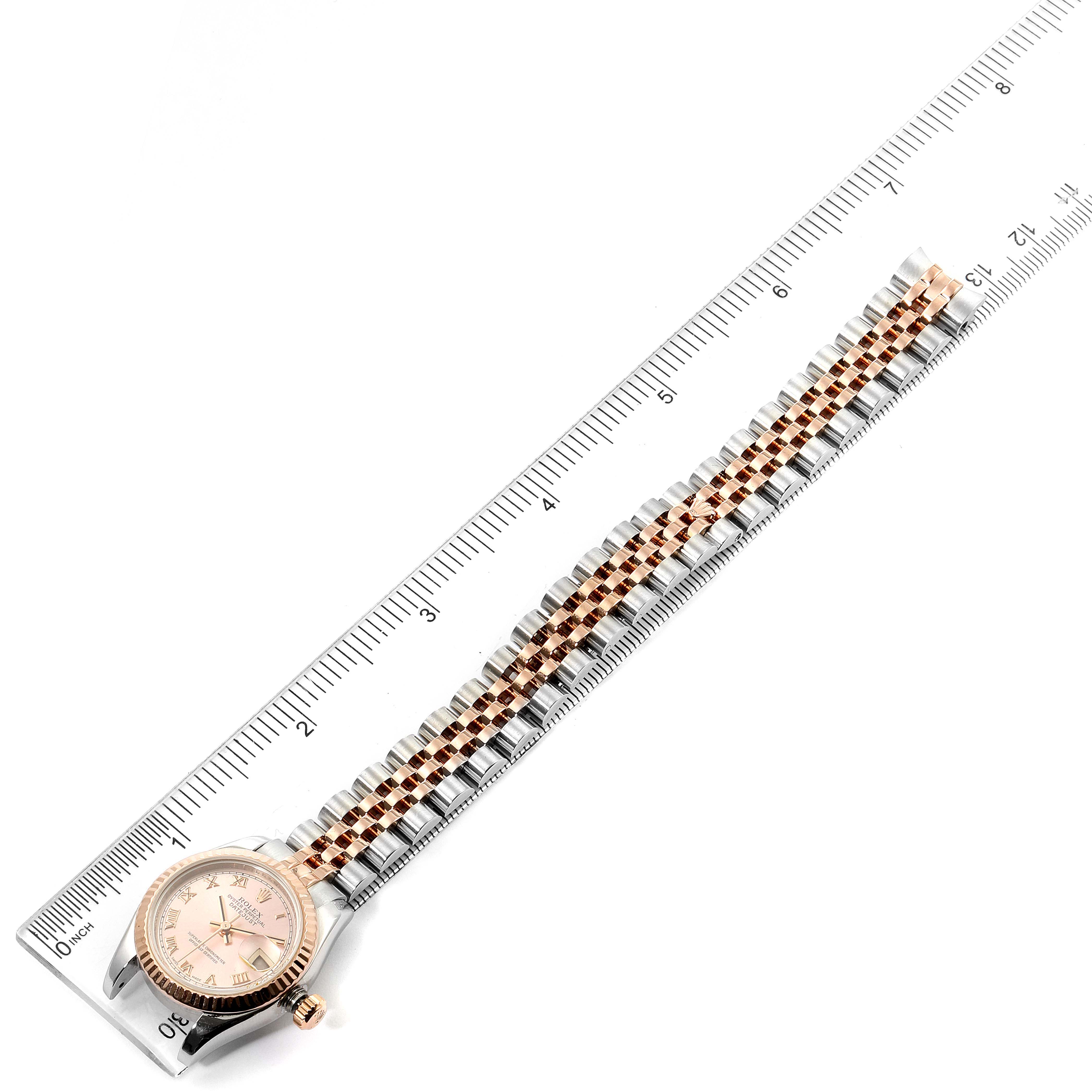 The Rolex Datejust 179171 Women's Rose Gold Pink Dial 179171 Women's Rose Gold Pink Dial watch is positioned flat, showing the full length of the bracelet next to a ruler for scale.